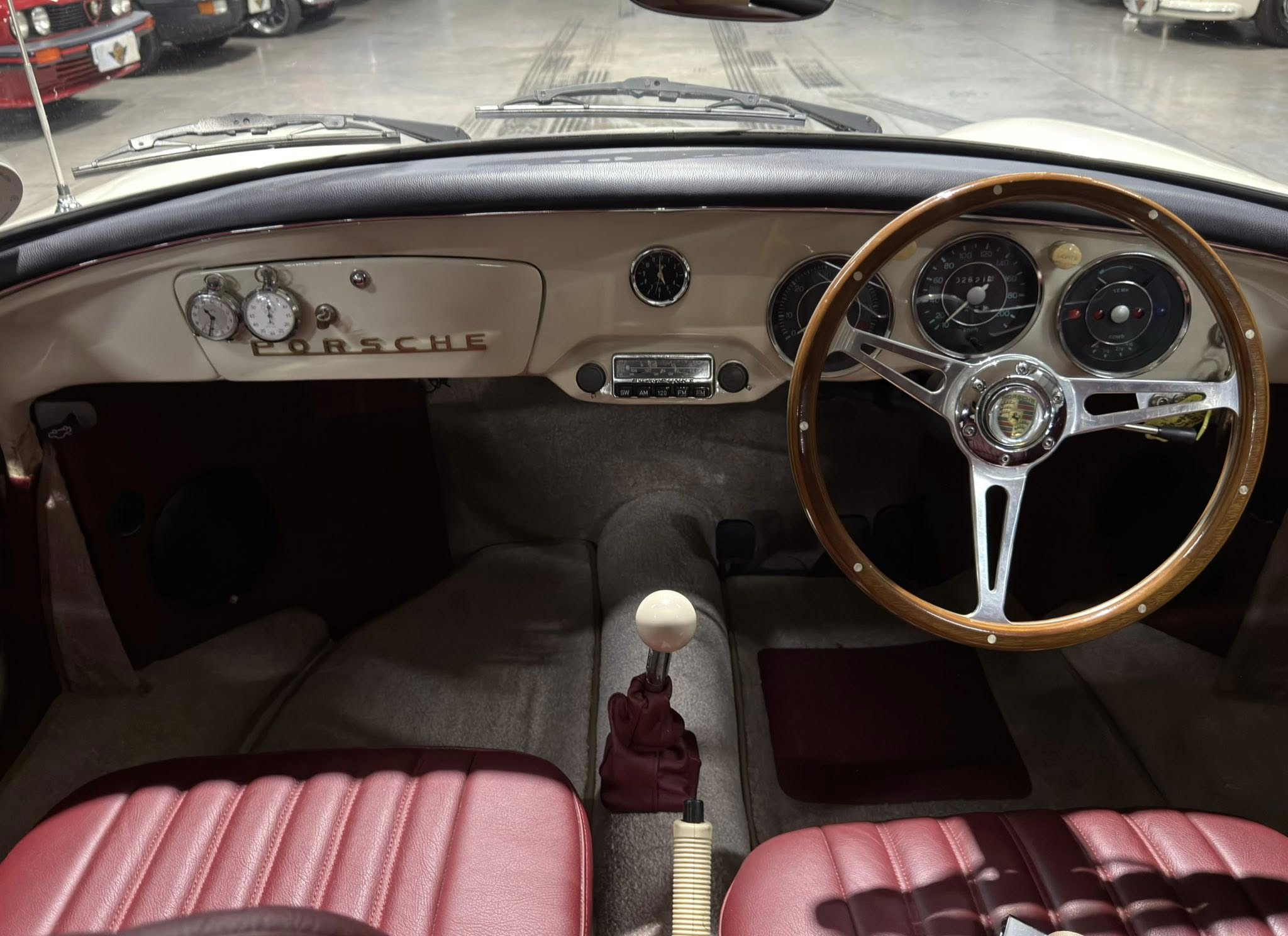 Classic Porsche interior from the driver's seat: beige dash, wood steering wheel, and red leather seats with analog gauges.