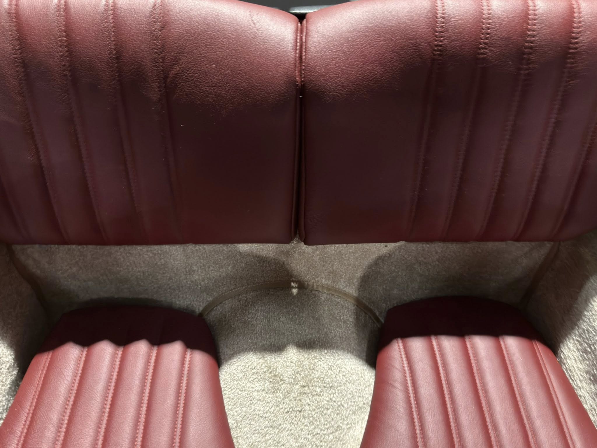 Close-up of pink leather upholstery with vertical stitched channels and a central seam where two pieces meet.