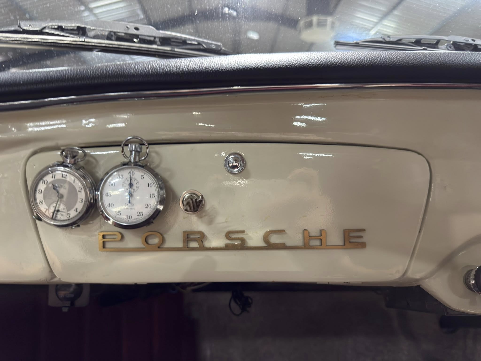 Interior of a vintage Porsche showing round gauge dials and the Porsche emblem on the beige dashboard