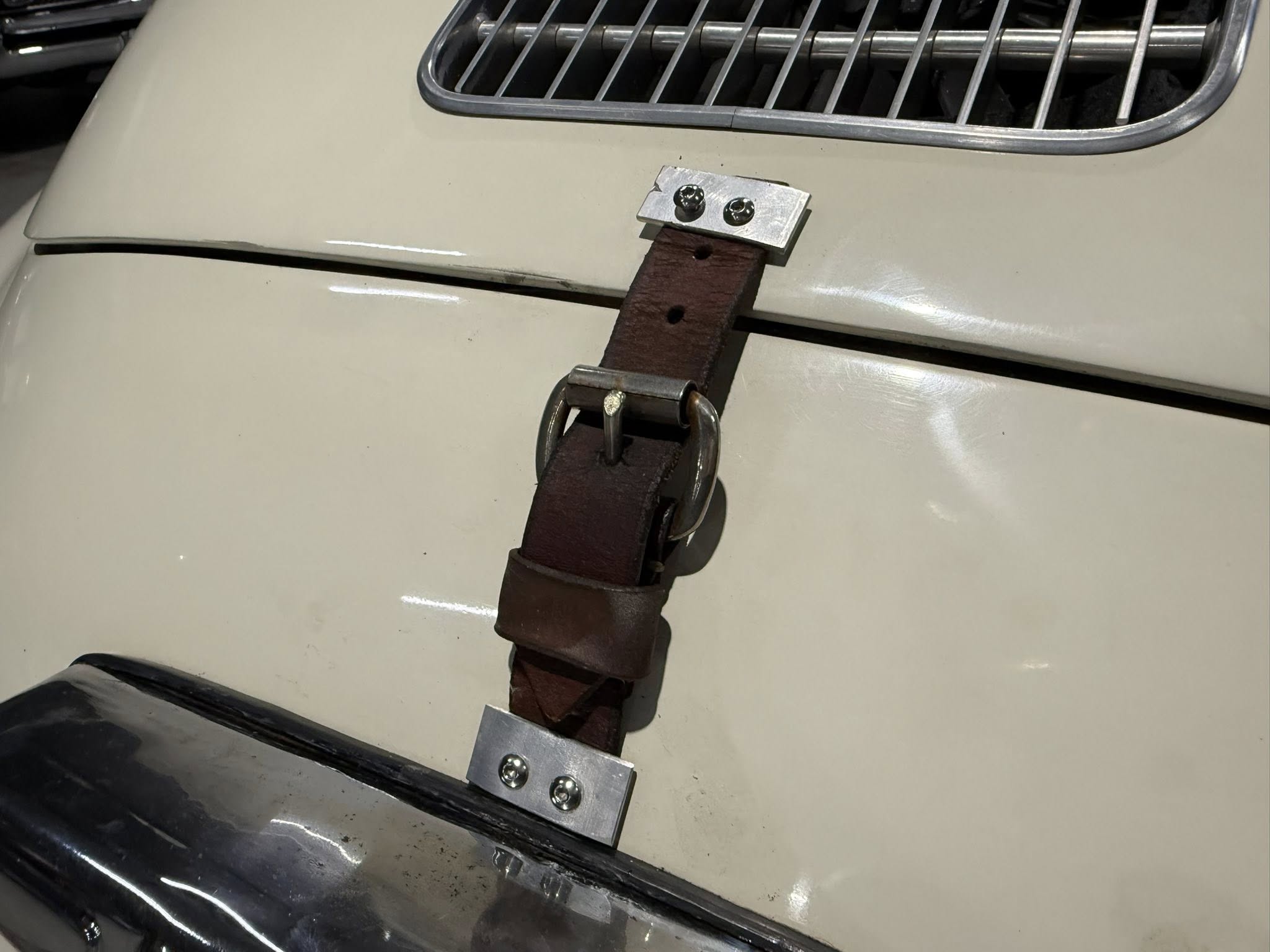 Close-up of a brown leather strap secured by metal brackets and bolts on a light-colored surface, with a chrome grille above.