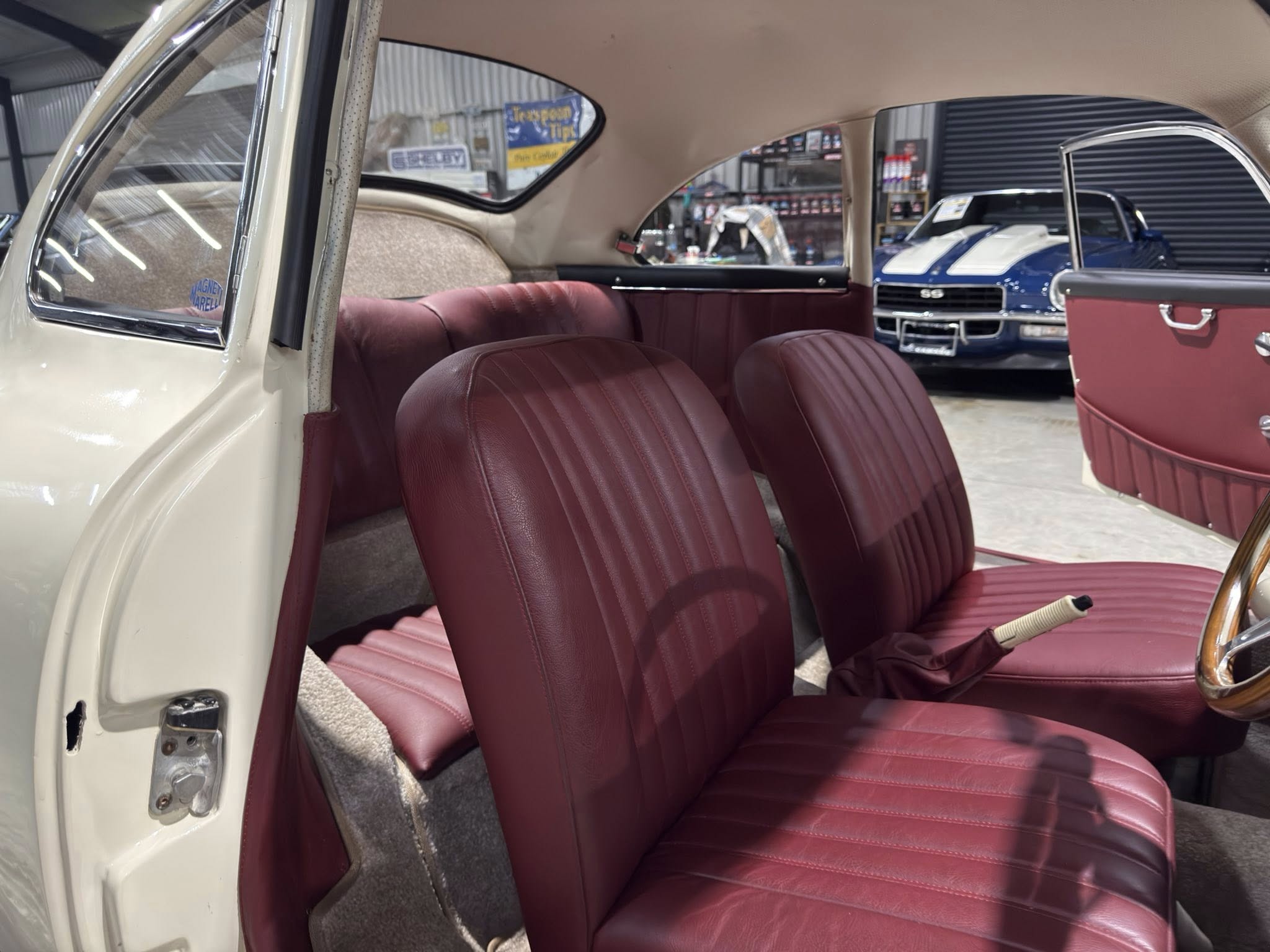 Interior of a vintage car with burgundy seats and beige trim, open door showing the door latch area in a showroom.