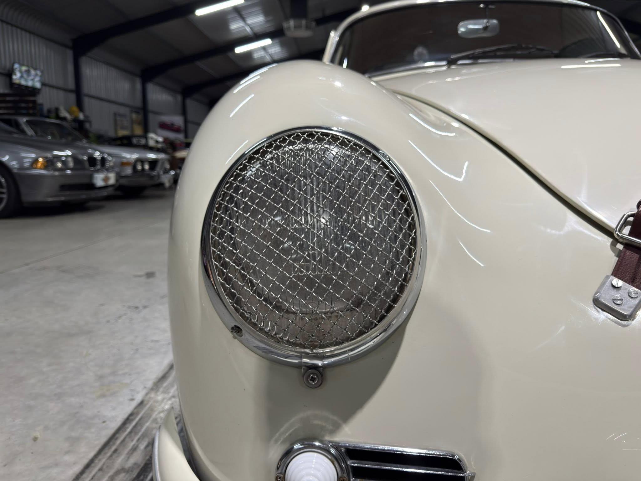 Close-up of a cream-colored vintage car front featuring a large circular mesh grille and chrome trim in a showroom setting.