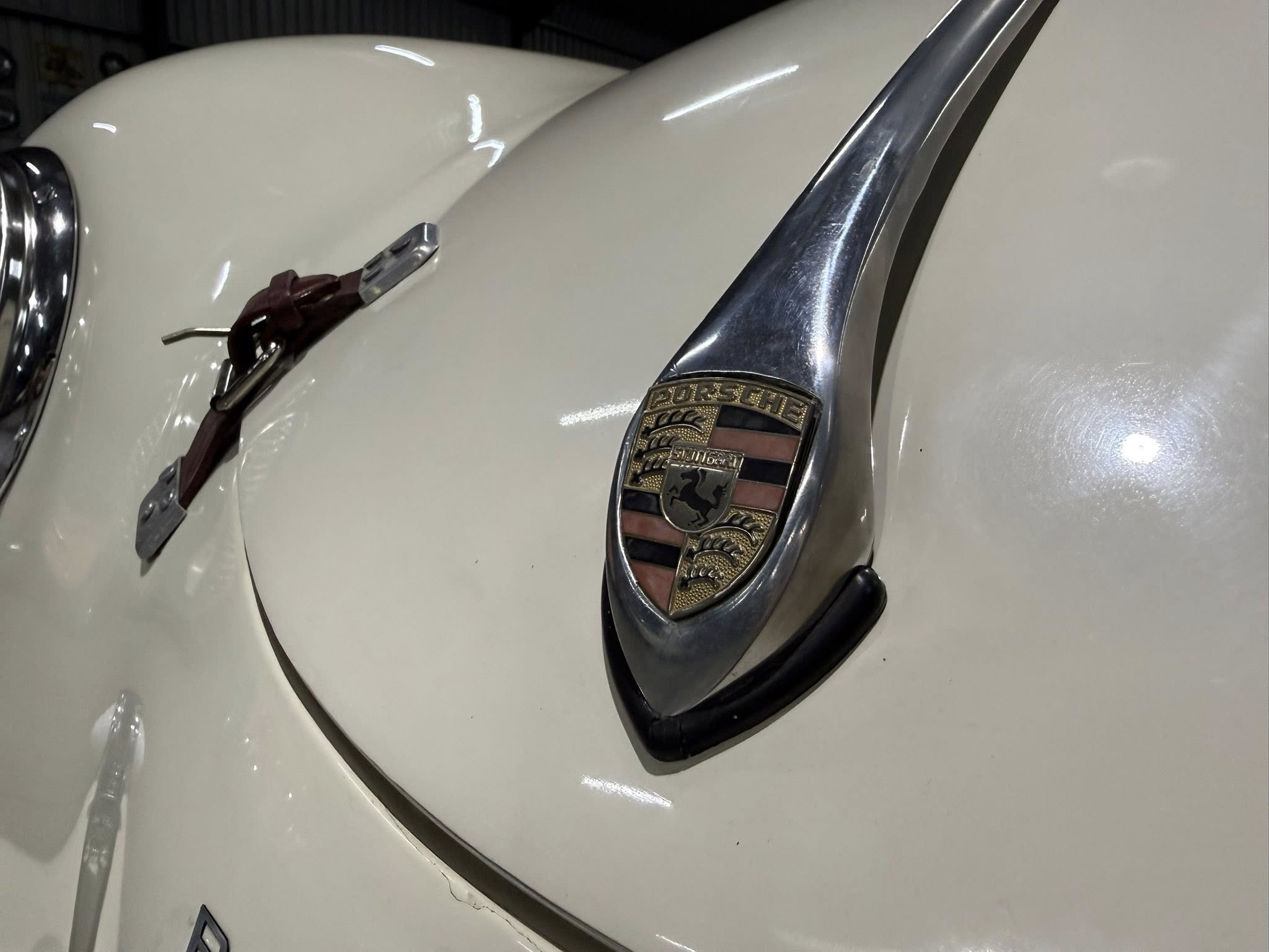 Close-up of a white Porsche hood with the gold crest emblem and chrome trim visible on the front edge of a classic car