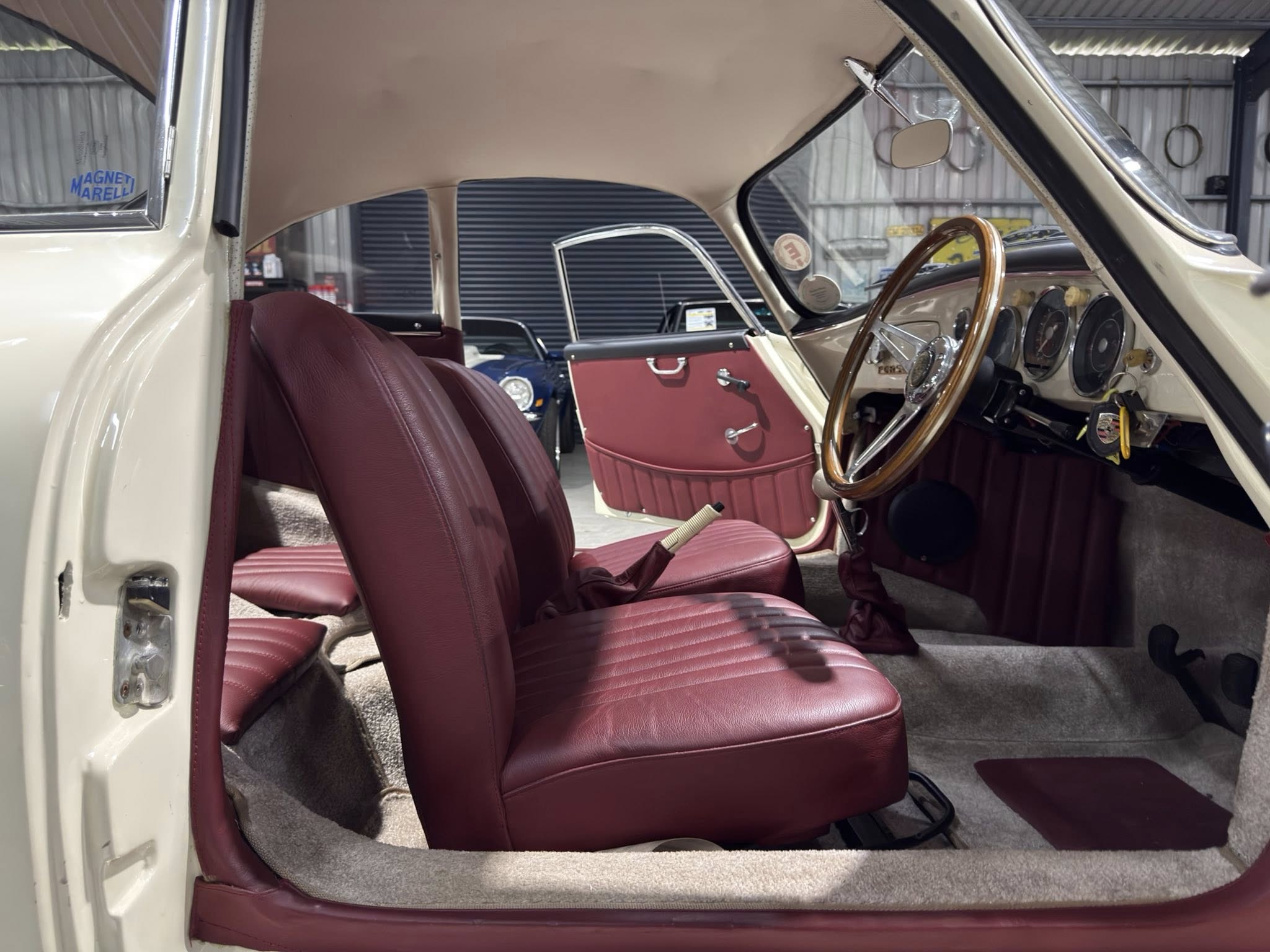 Interior of a vintage car with red leather seats, beige headliner, and a wooden steering wheel.