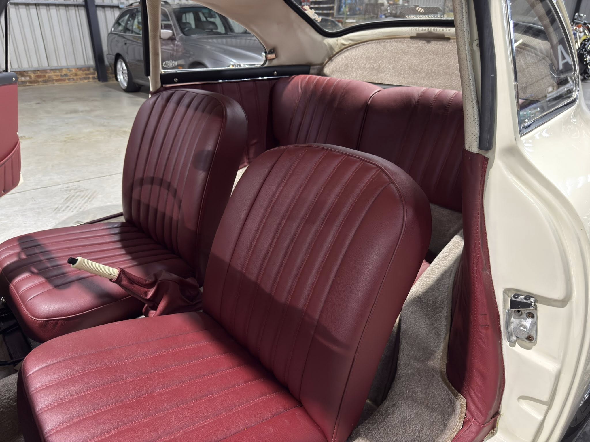 Interior of a vintage car with red leather seats and beige headliner, open door showing the outside area.**