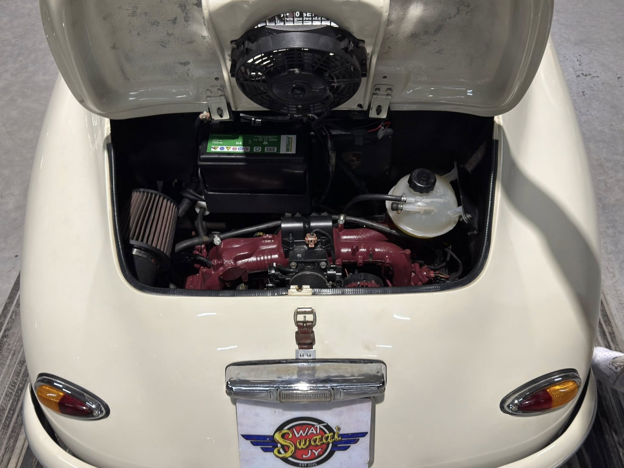 Open rear hood reveals scooter engine bay with fan, battery, and red engine block visible under the hood.