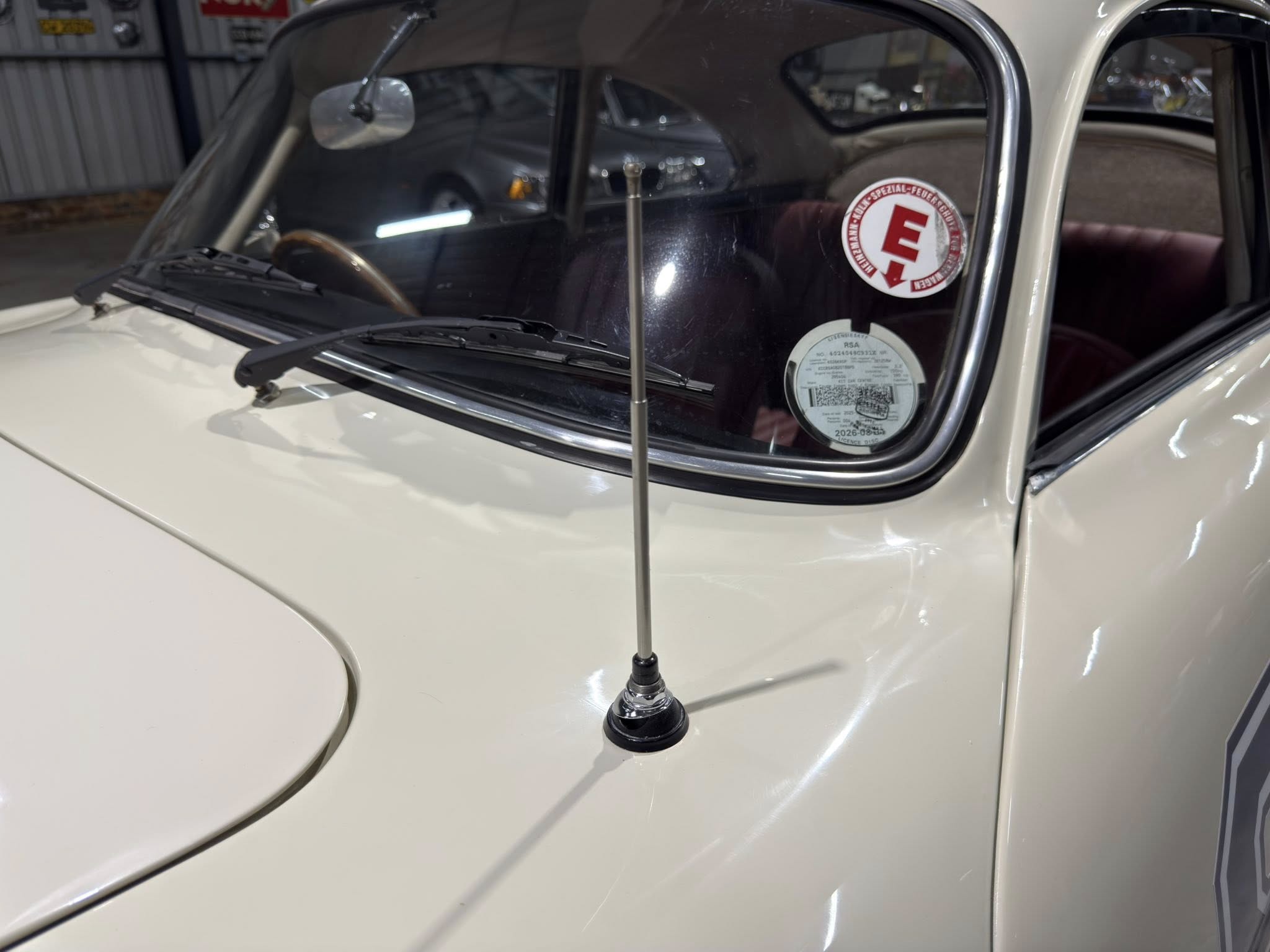 Close-up of a vintage car's windshield and hood, with a tall antenna and sticker on the glass.