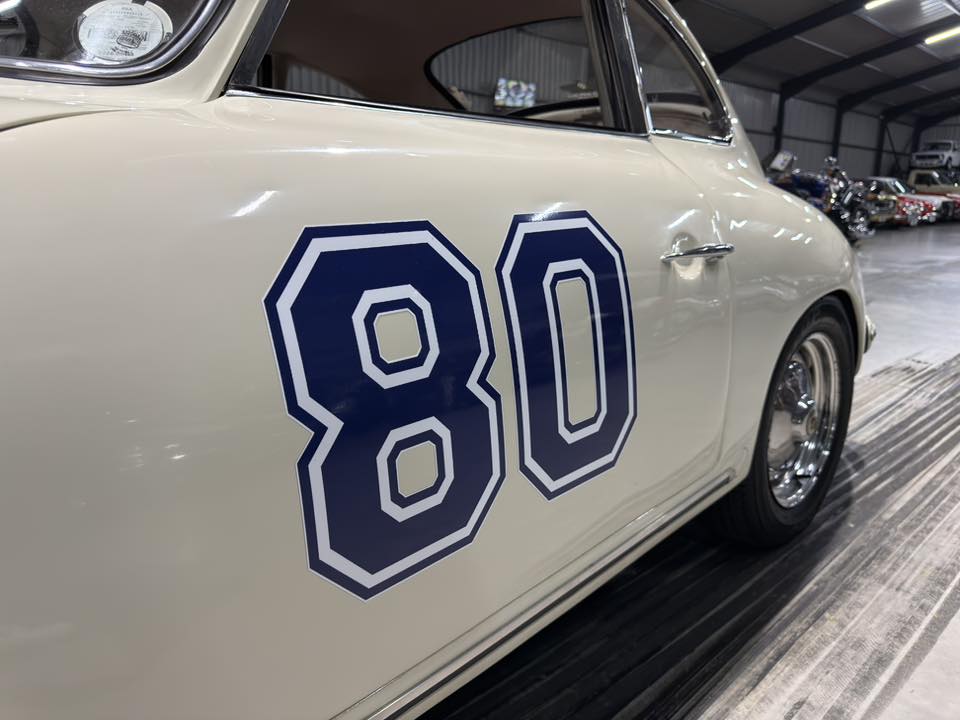 Classic white race car with bold blue number 80 on its door, parked in a museum-like showroom.