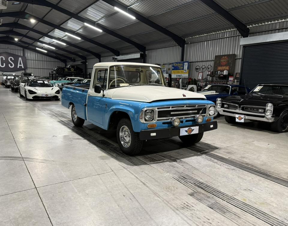 Front view of a two-tone blue and white vintage pickup truck on display in a well-lit showroom with other classic cars nearby.