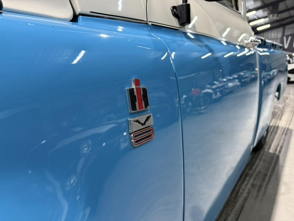 Close-up of a blue vintage car door with chrome emblem badges.