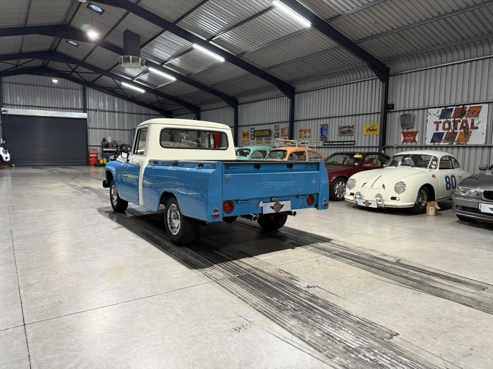 Blue and white vintage pickup parked inside a bright showroom with other classic cars along the wall.