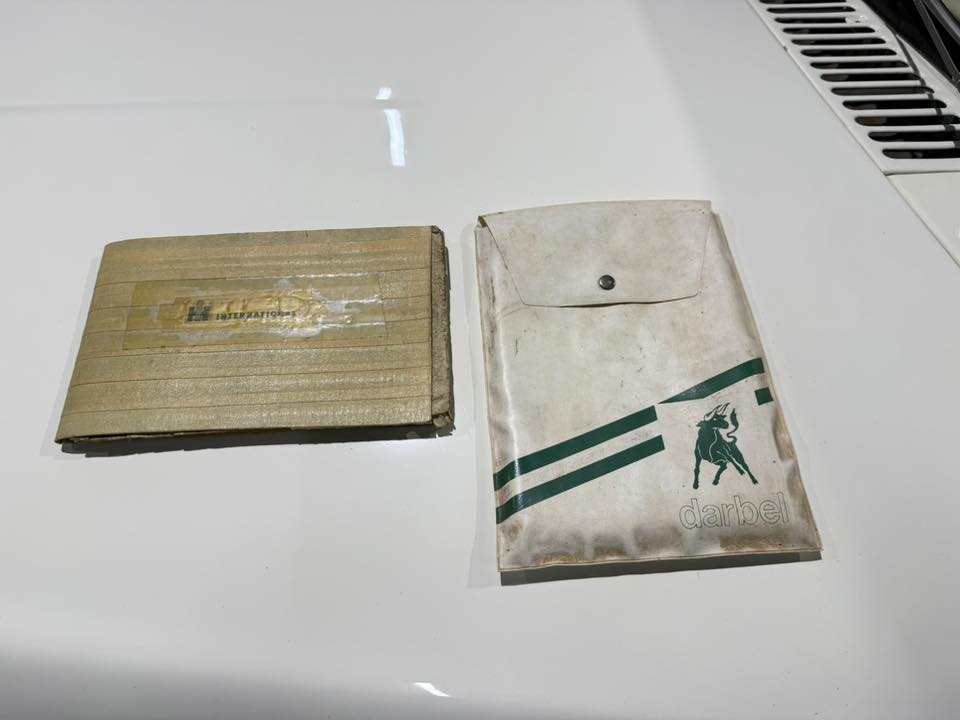 Two old envelopes on a white car hood: a brown corrugated mailer and a white Darbel envelope with green stripes and a horse logo.