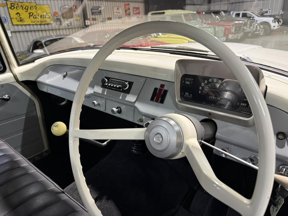 Interior of a vintage car with a cream steering wheel, gray dash, and classic gauges, seen from the driver's seat in a showroom .