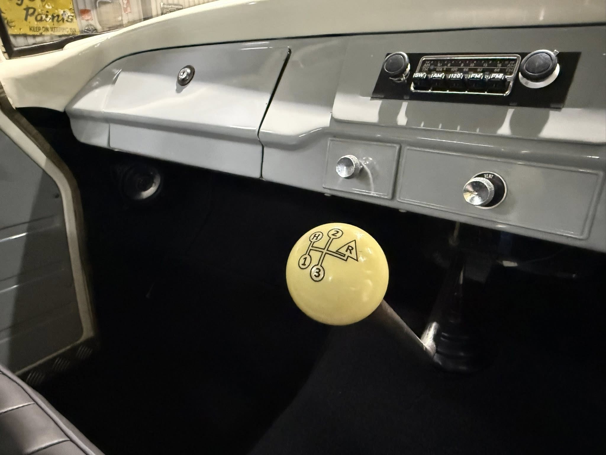 Close-up of a classic car dashboard with a retro radio and a yellow gear-shift knob showing 1-2-3 and R.