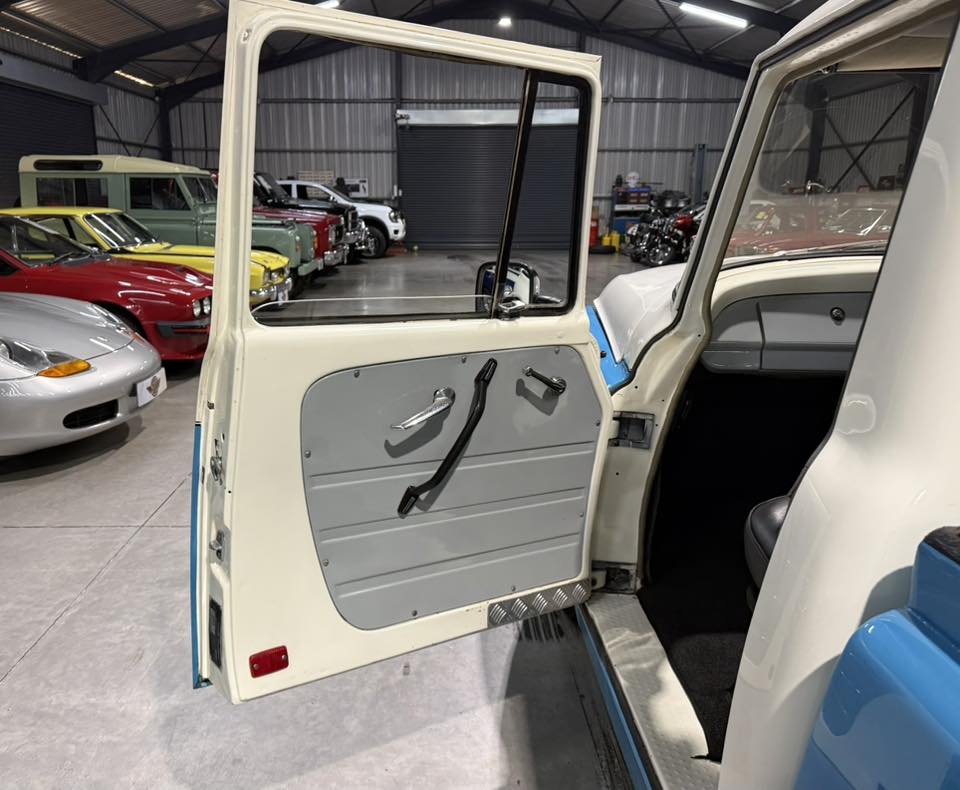 Open passenger door of a cream vintage truck in a showroom, showing the gray door panel and black handles.