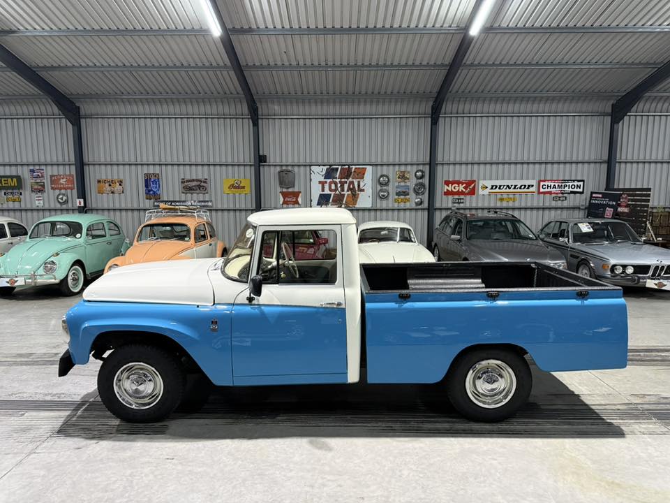 Blue and white vintage pickup truck parked in a metal-walled showroom with other classic cars in the background