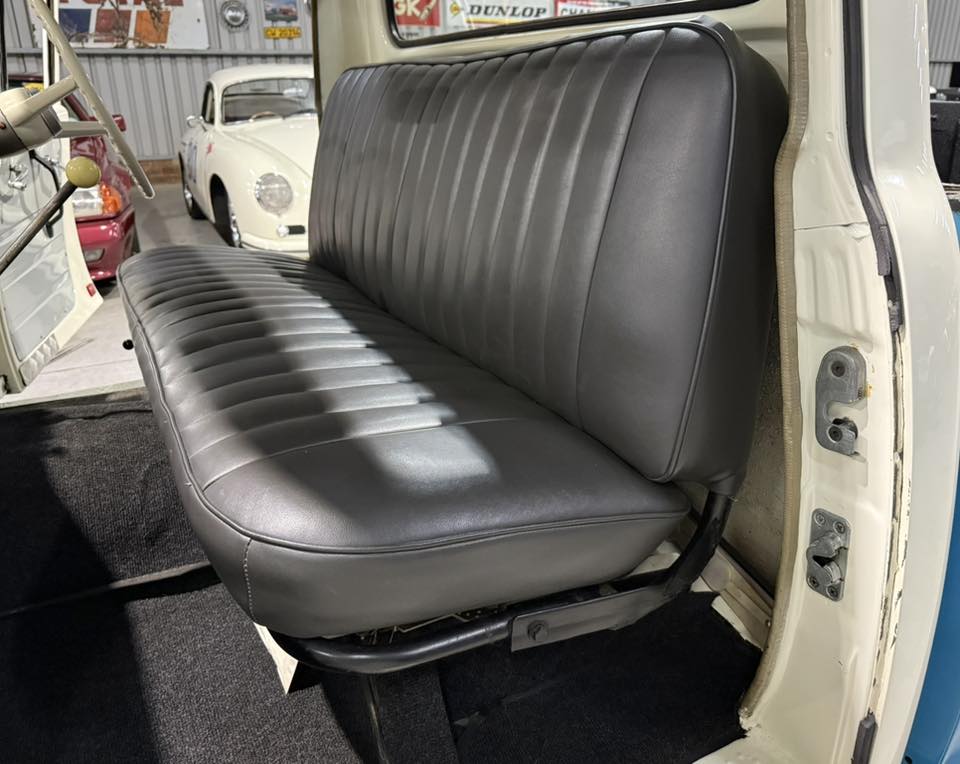 Black vinyl bench seat in a vintage pickup truck, door open and classic cars visible in the background.