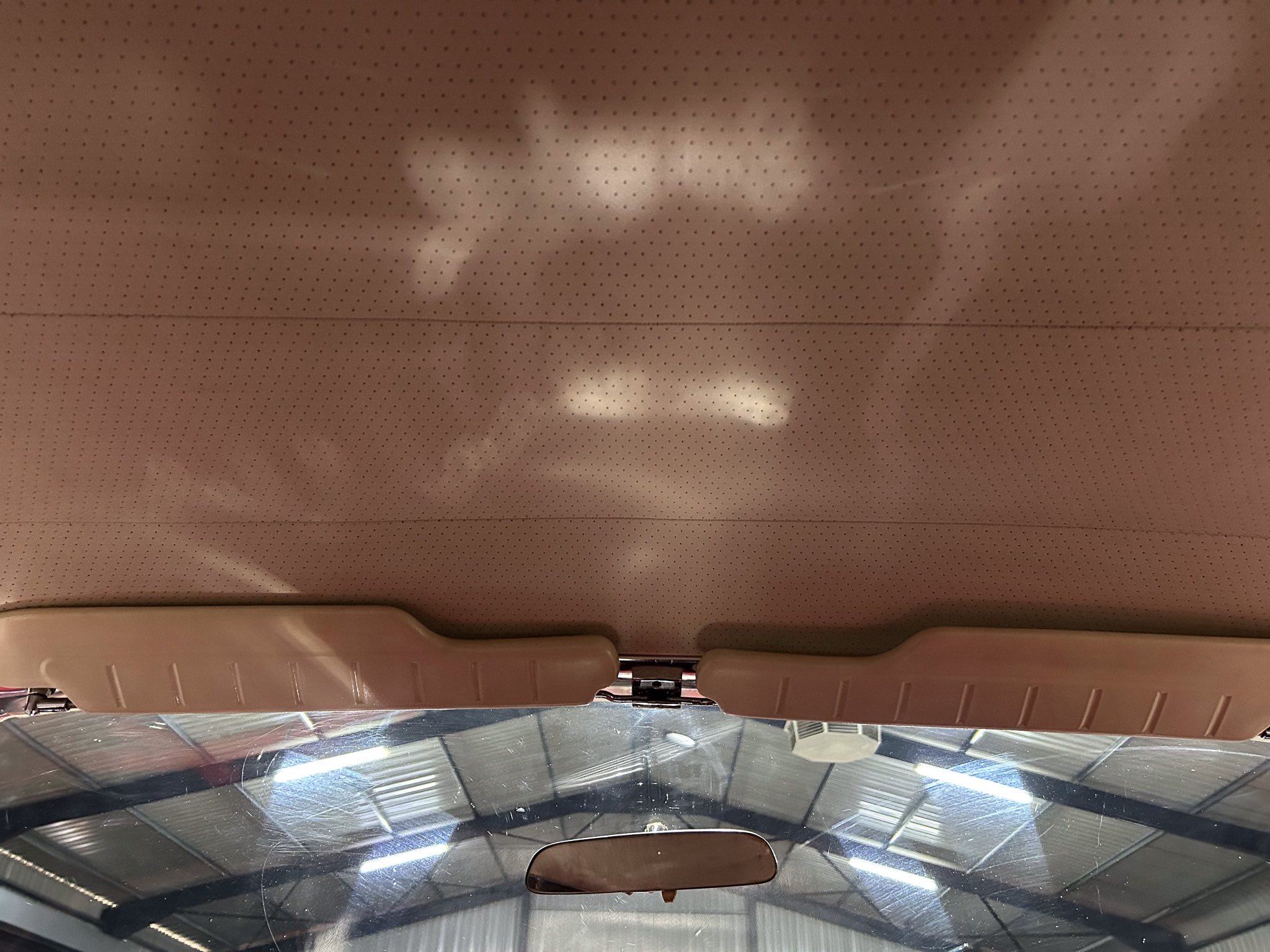 Tan perforated car headliner with two beige sun visors, rearview mirror, and windshield visible.