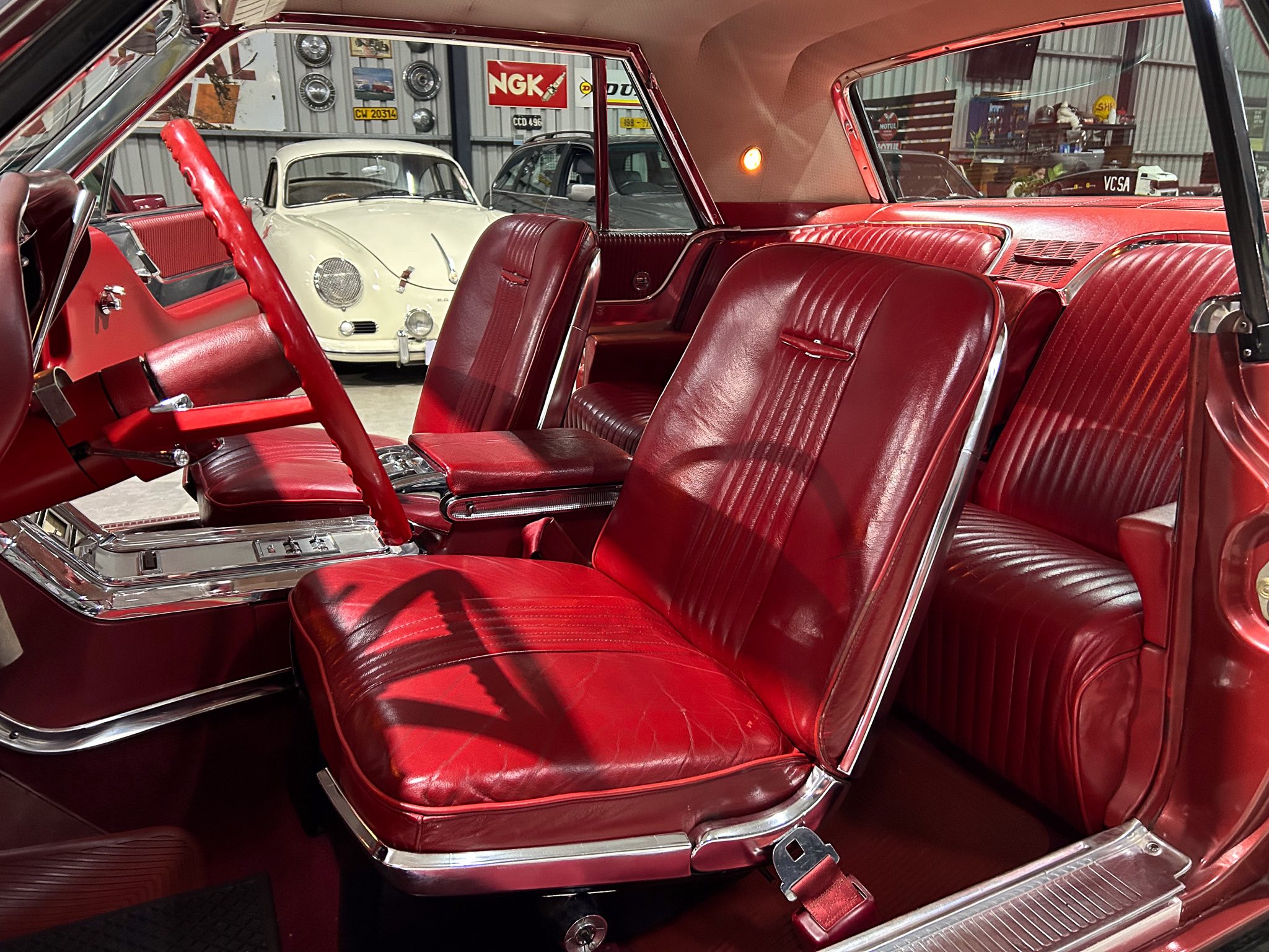 Red leather interior of a vintage car with chrome trim and a red steering wheel, view of the front seats inside a showroom.