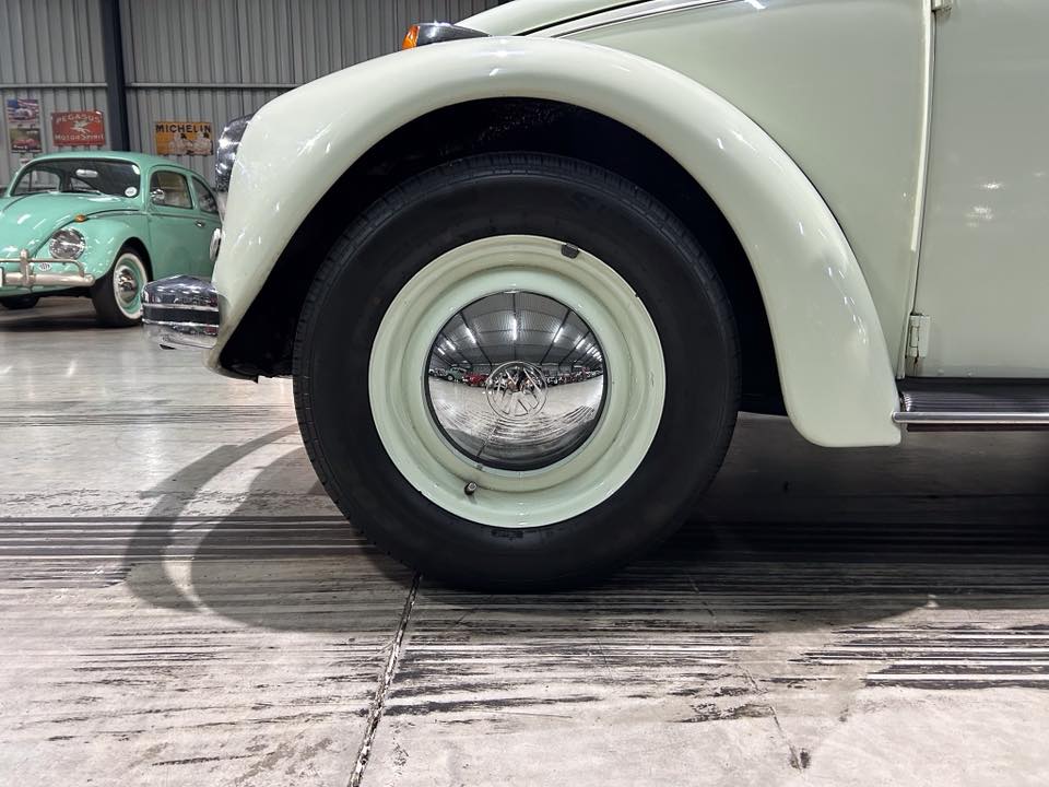 Close-up of a pale mint vintage car wheel and fender with a chrome hubcap; other classic cars visible in a showroom background.