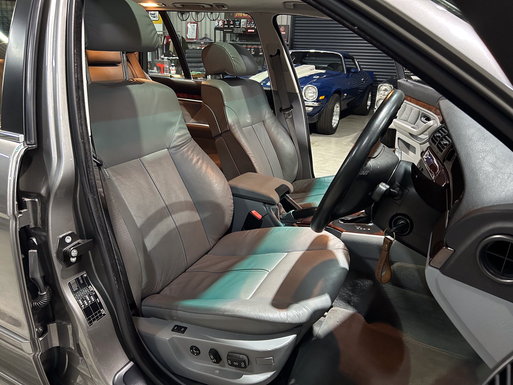 View of the car's front interior: right-hand drive cockpit with gray leather seats, steering wheel, and center console.