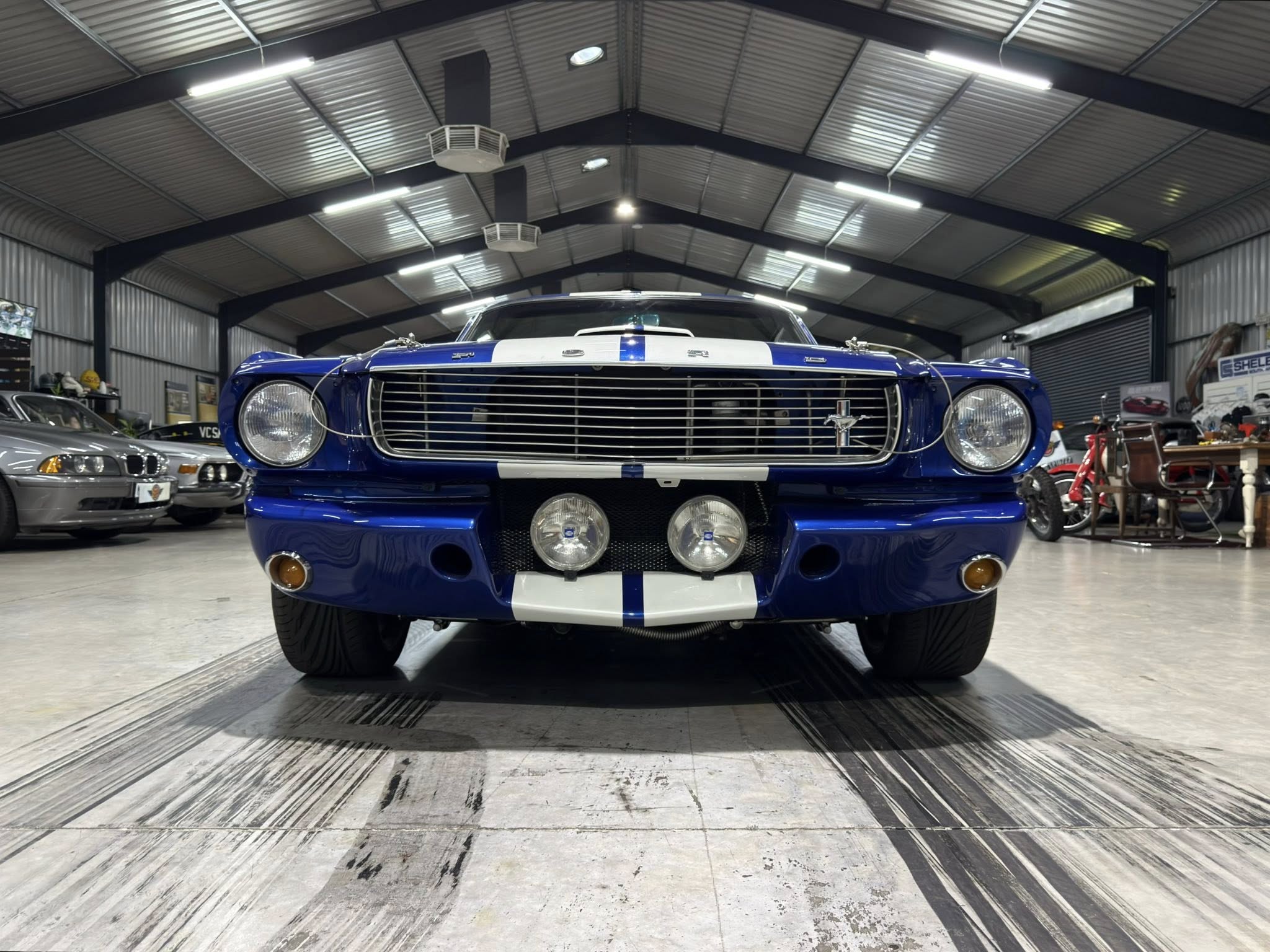 Front view of a blue vintage Ford Mustang with white racing stripes in a showroom garage showroom setting.