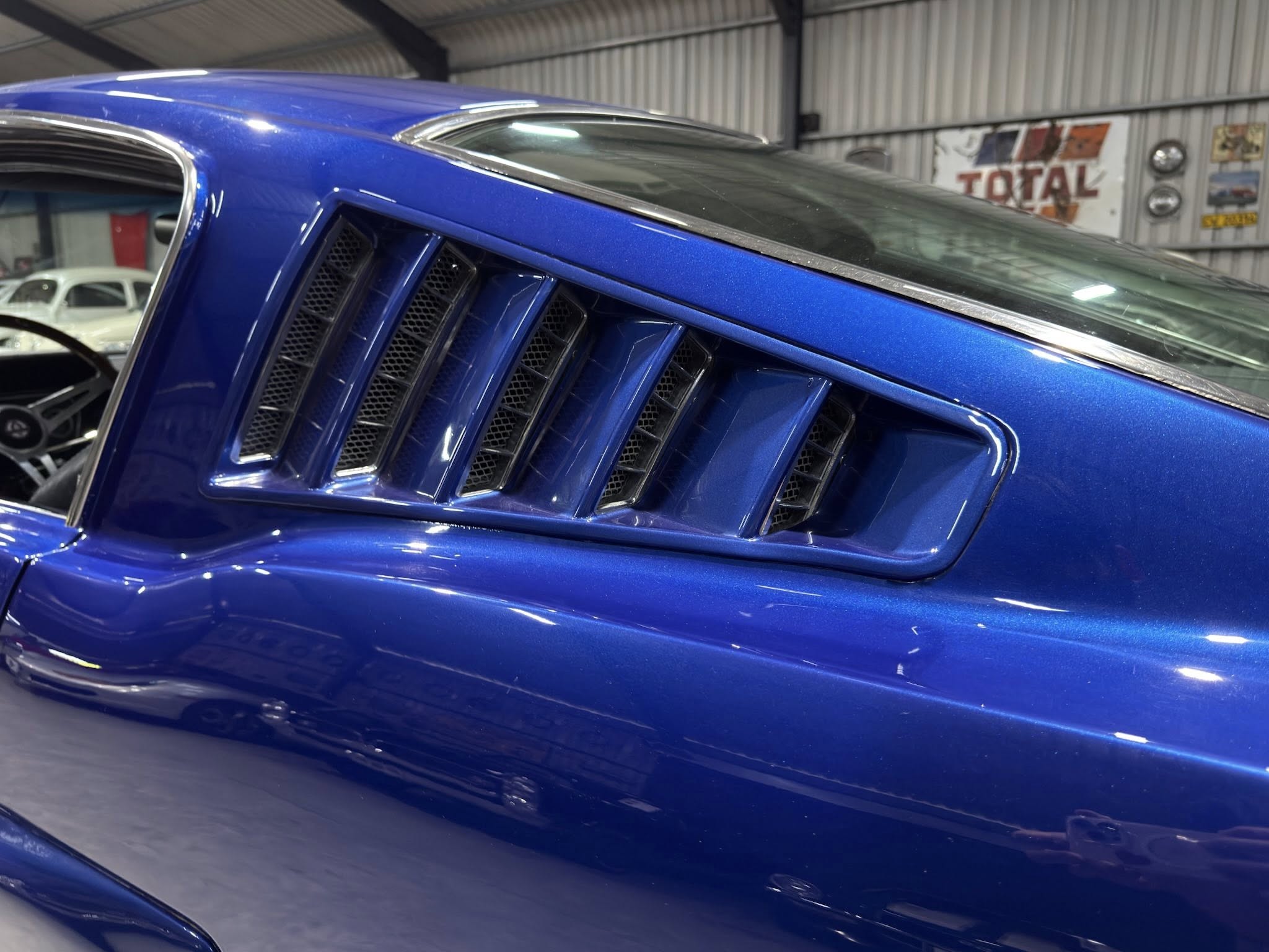 Close-up of a metallic blue car’s front end with vented grille in an indoor showroom or garage