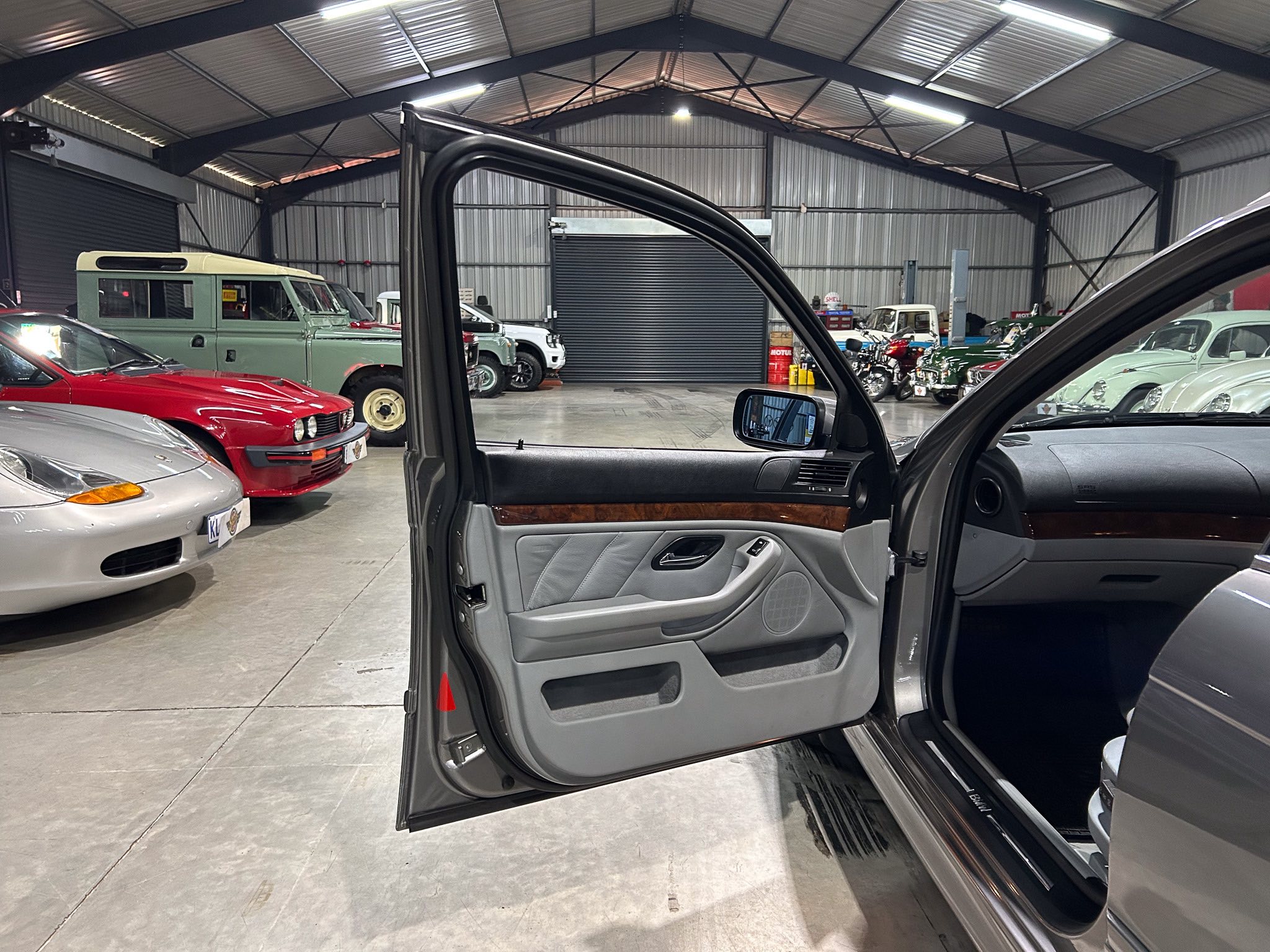 Open car door of a dark SUV in a large showroom filled with vintage cars and motorcycles in the background.