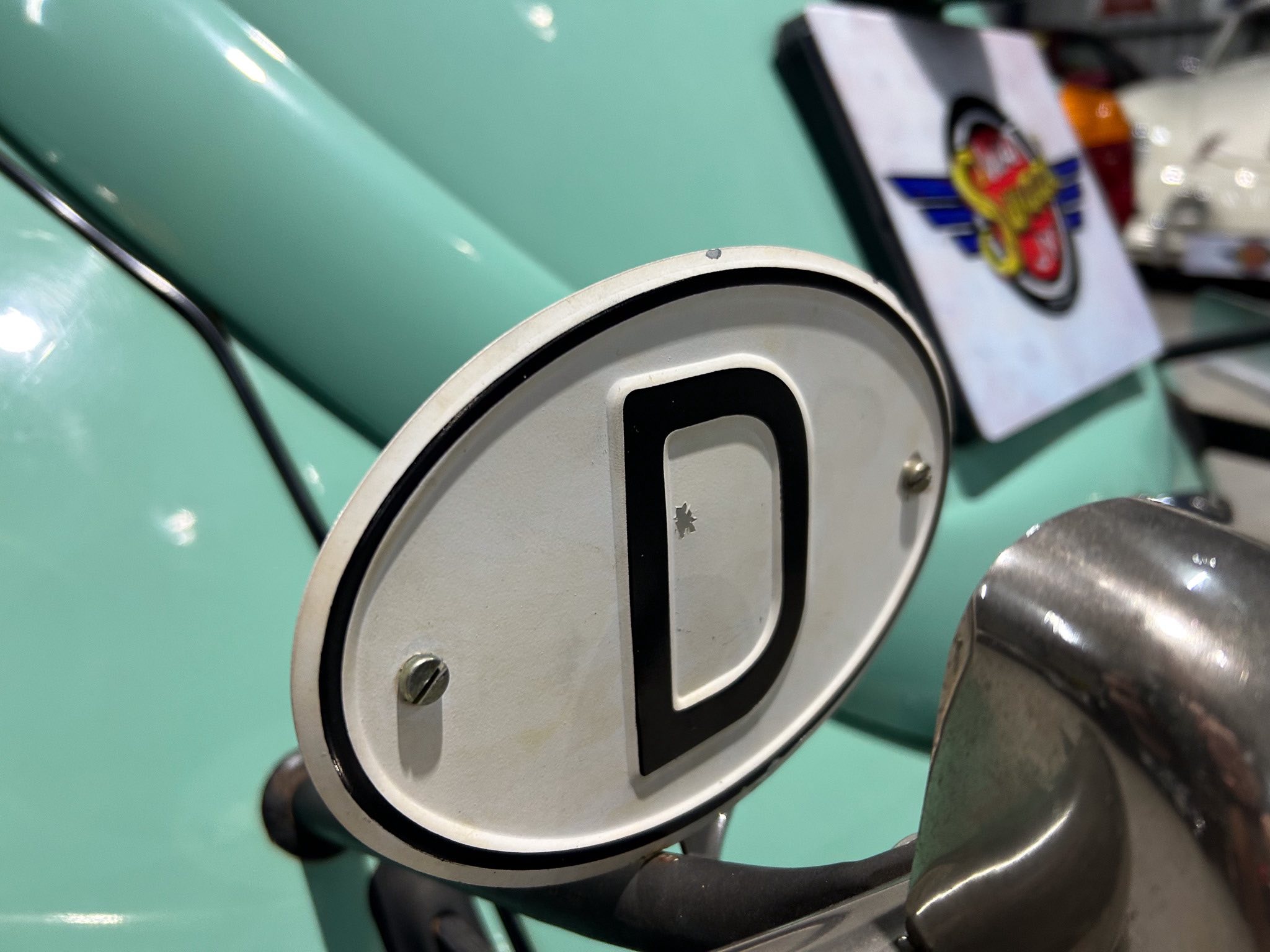 Close-up of a vintage mint-green motorcycle fuel tank with a large circular gauge in the foreground.