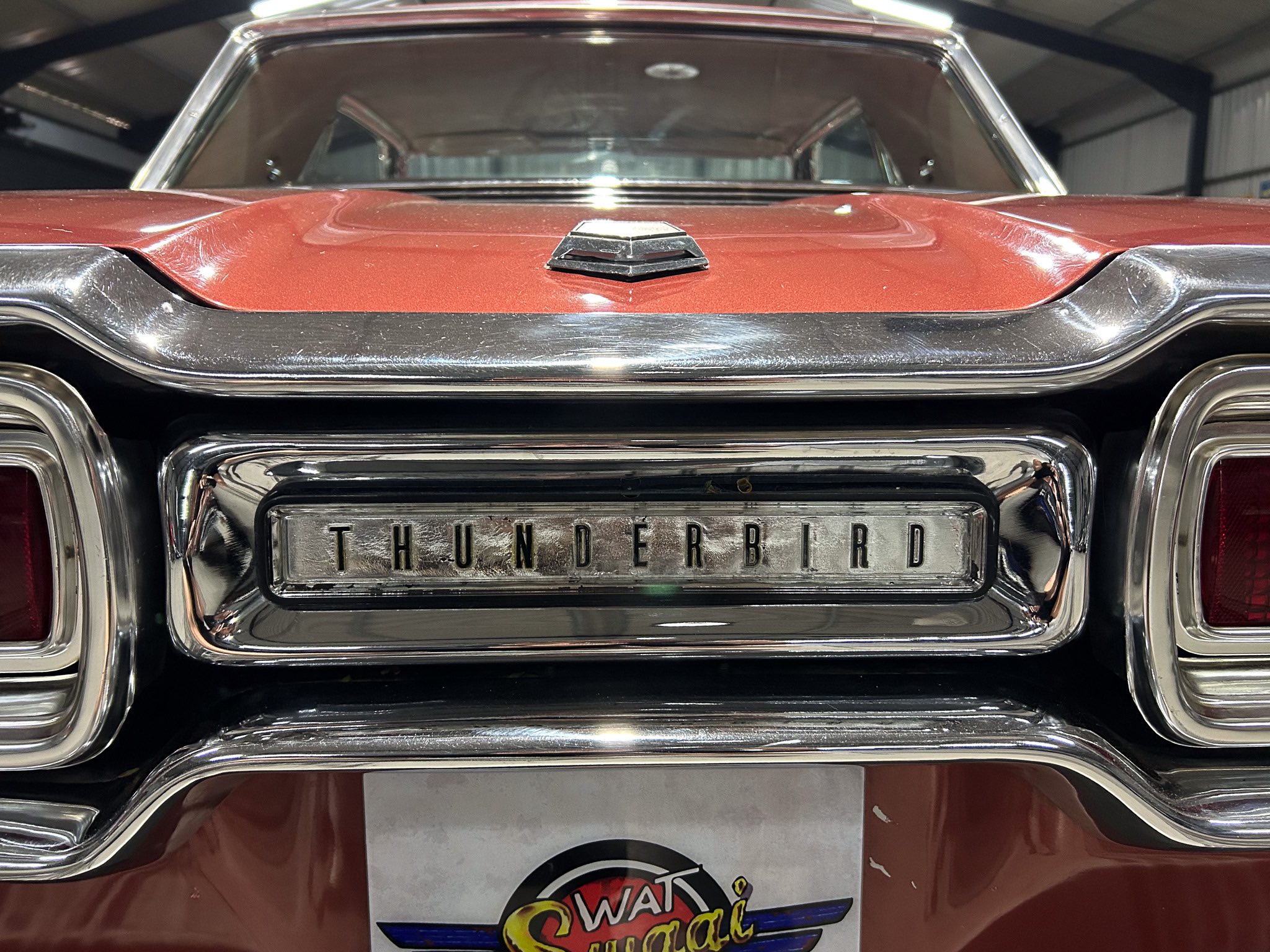 Rear view of a vintage red car with a chrome bumper and 'Thunderbird' license plate, in a showroom setting.