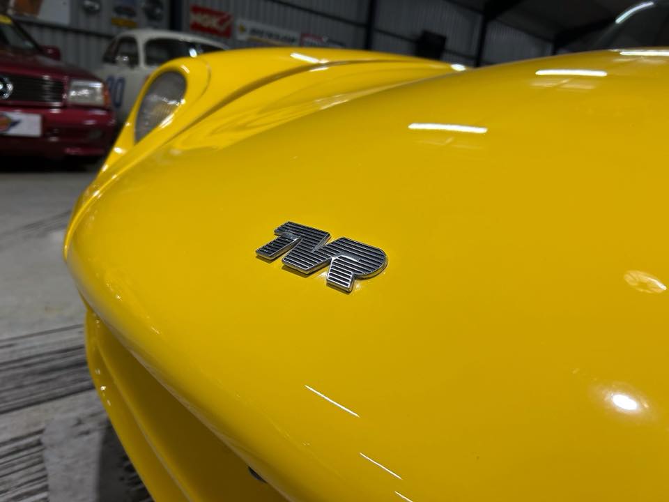Close-up of a bright yellow car hood with a chrome 'MR' badge.