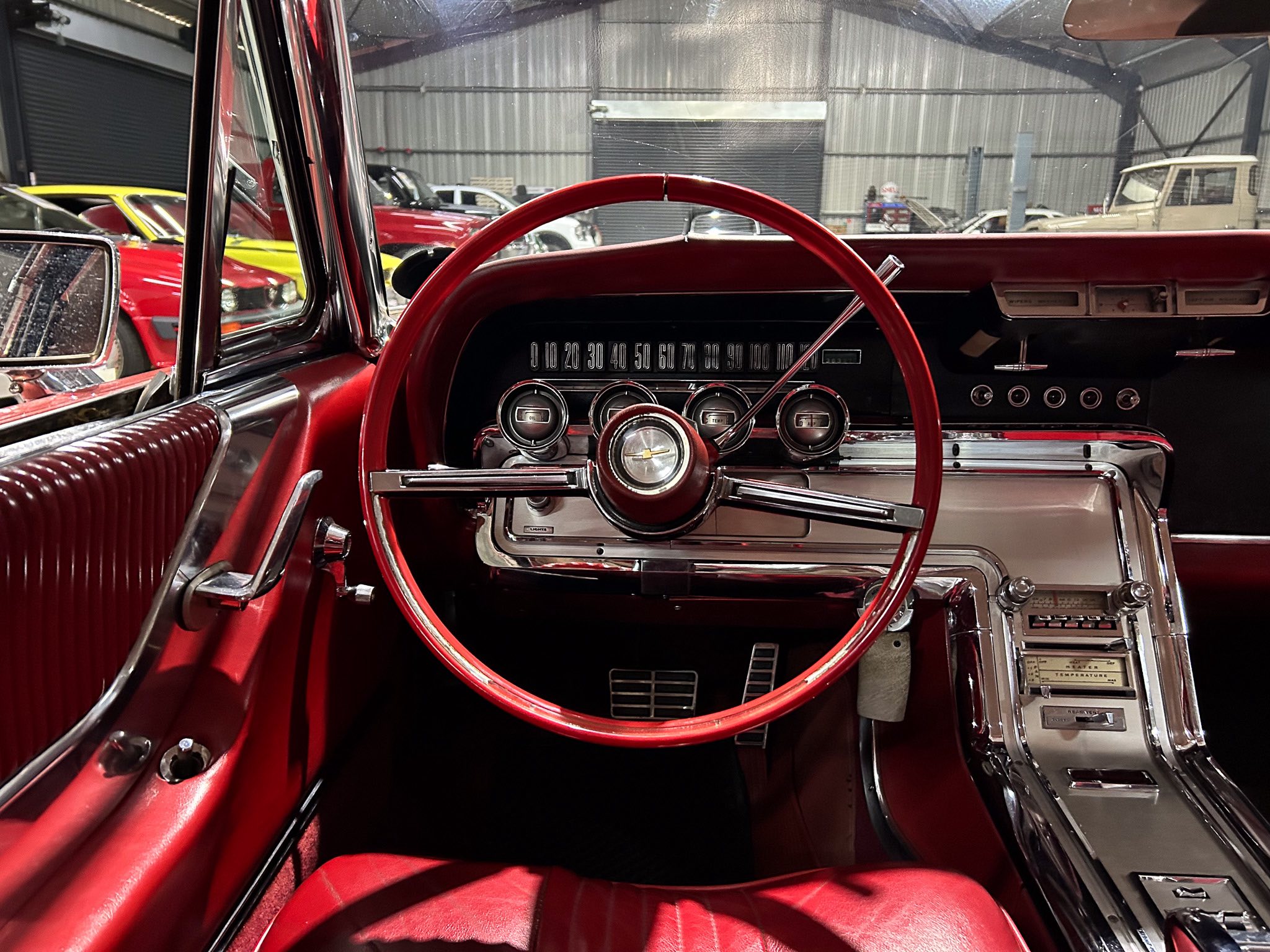 Red vintage car interior with a chrome dashboard, large circular gauges, and a red steering wheel.