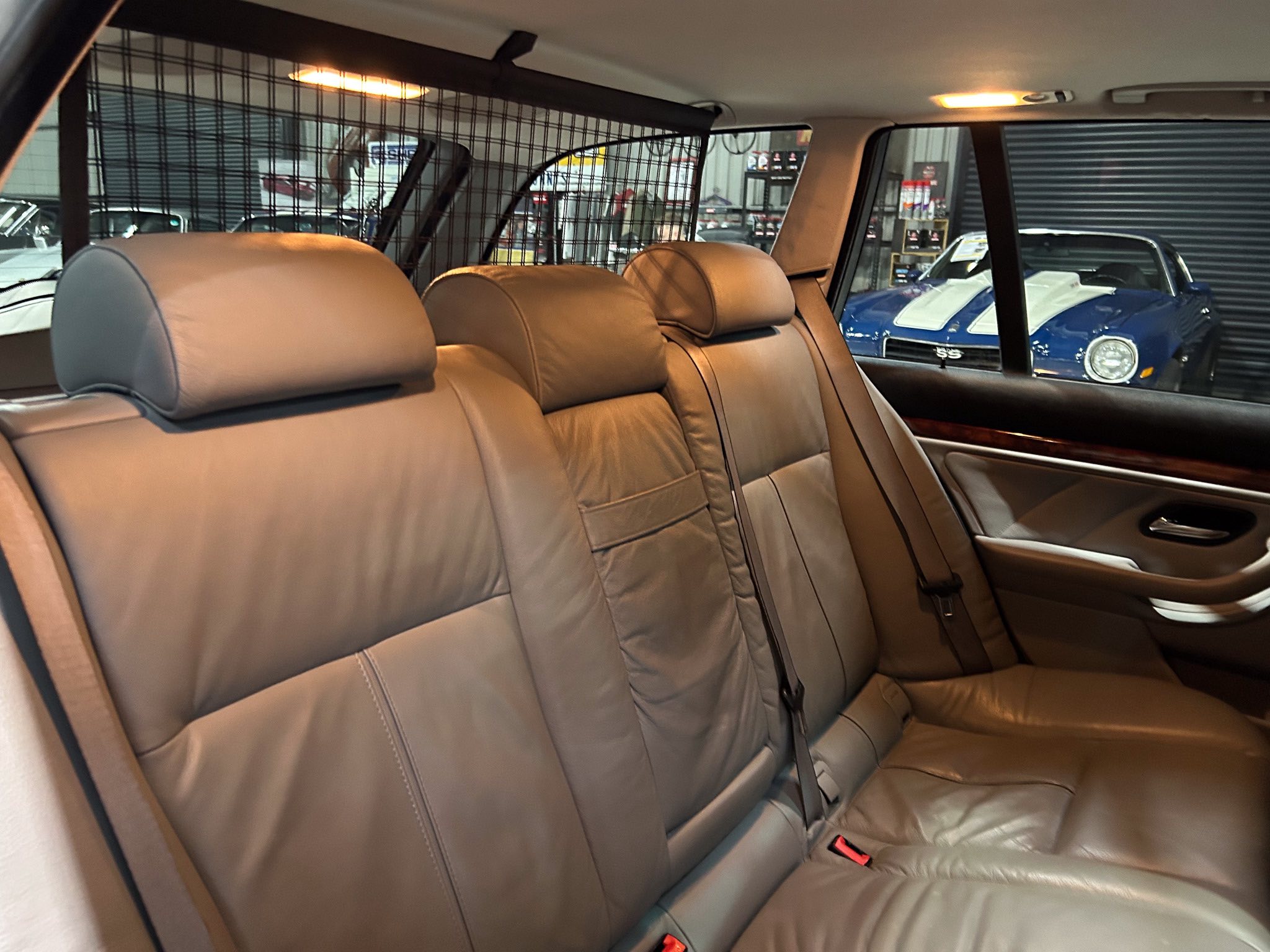 Beige leather backseat of a car with a metal mesh partition and a blue classic car visible through the rear window outside the vehicle