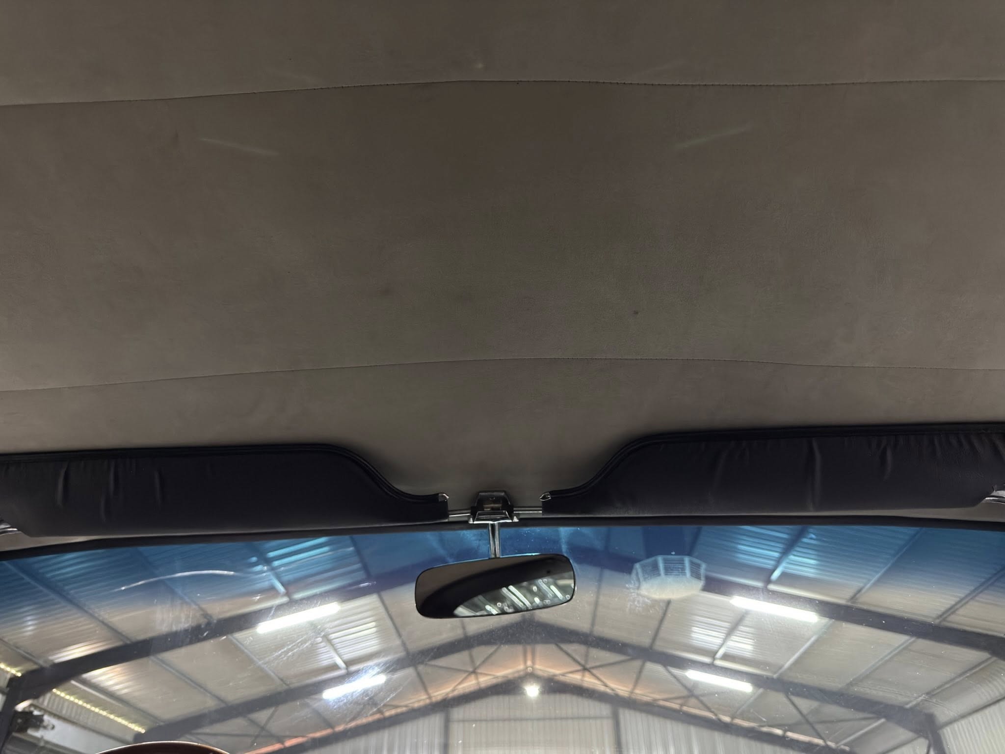 Interior view of a car ceiling showing a dark headliner, overhead area, and rearview mirror.