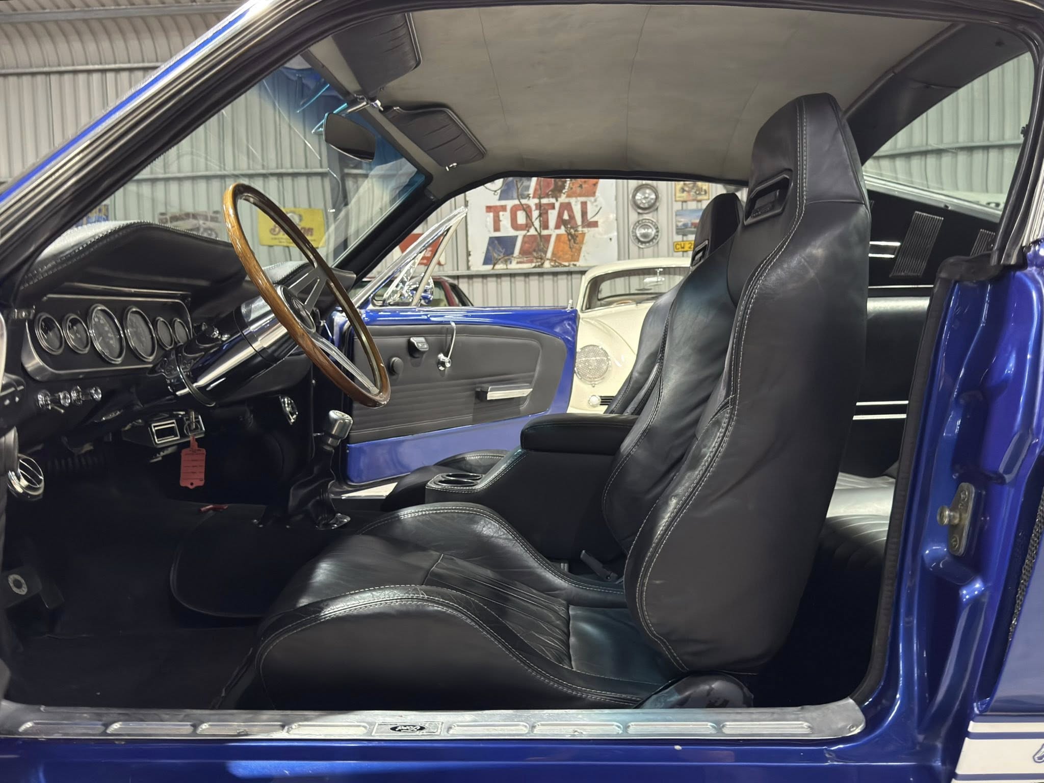 Interior of a blue vintage car showing a wooden steering wheel, black leather seats, and chrome-dial gauges on the dash