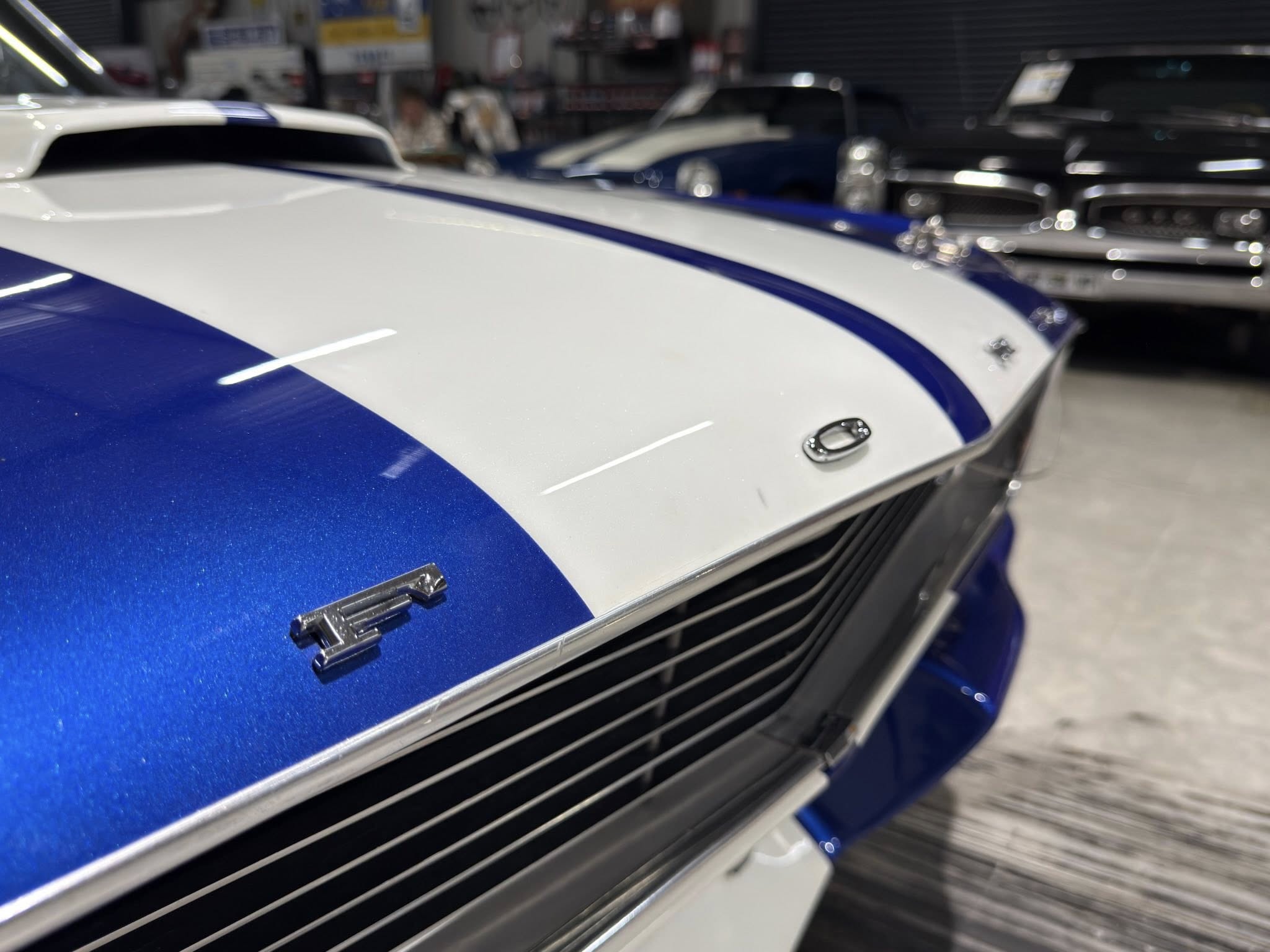 Close-up of a blue and white racing stripe on a car hood inside a showroom with other vehicles in the background.
