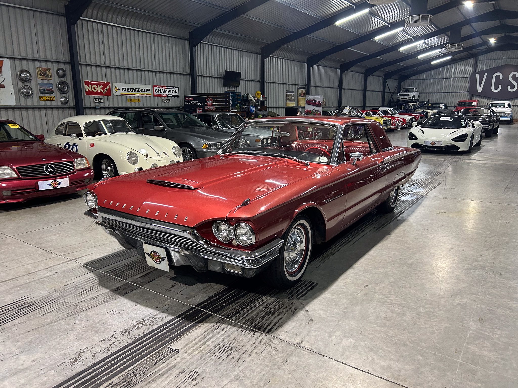 Indoor showroom filled with classic cars; a red convertible dominates the foreground with more vintage cars in the background.