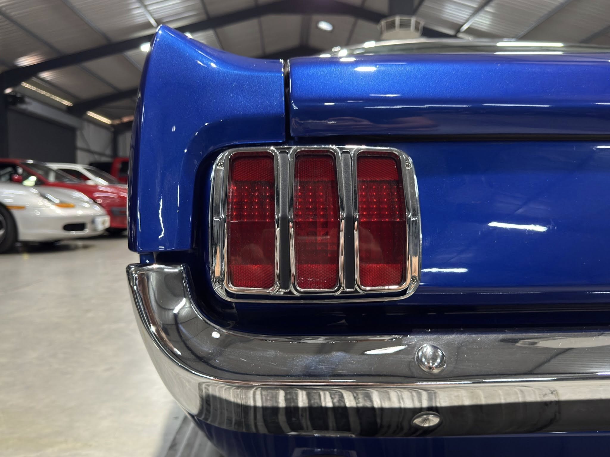 Close-up of a blue car's rear end, showing the triple taillight assembly with chrome trim in a showroom setting
