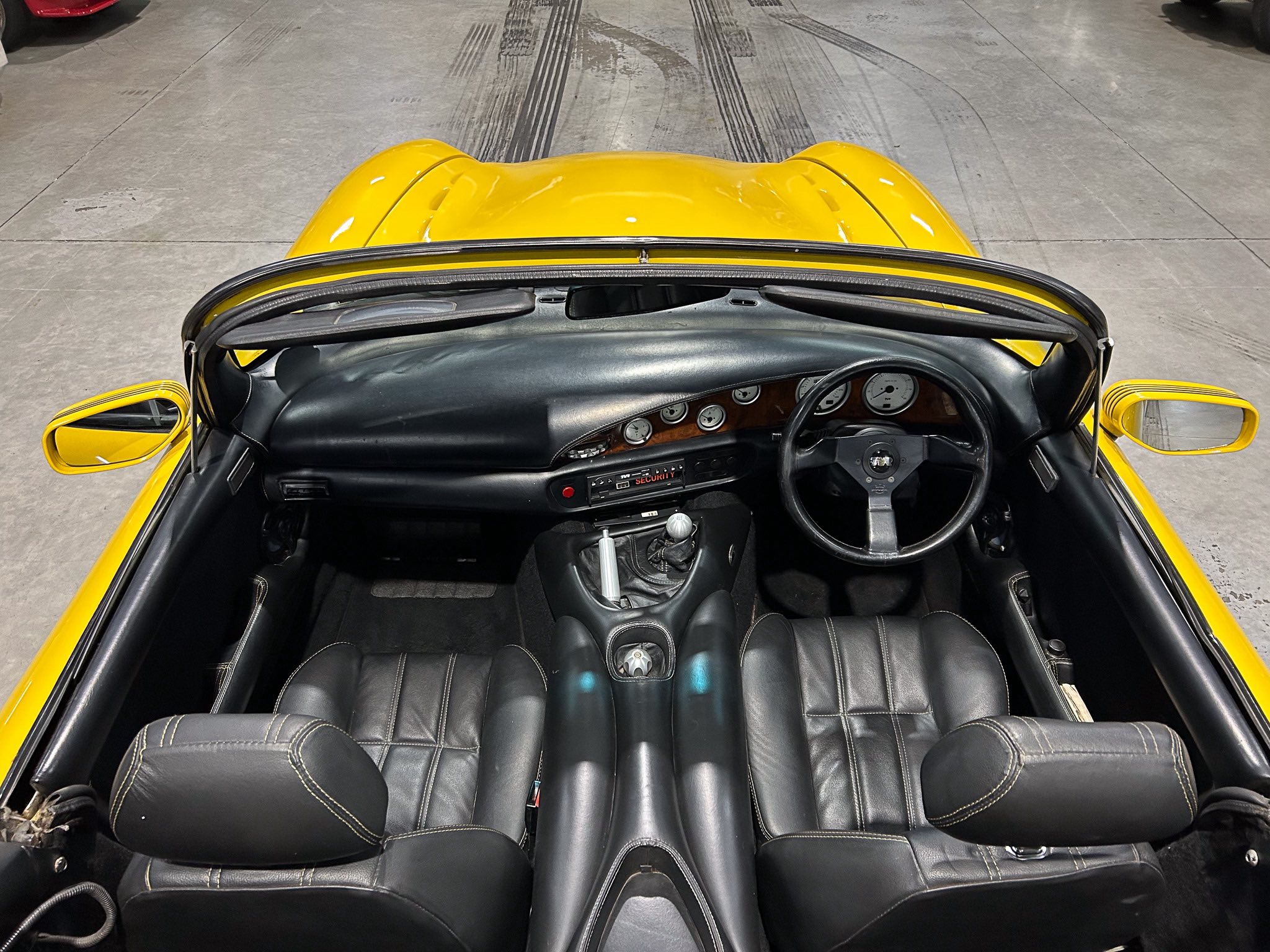 Overhead view of a yellow sports car interior with black leather seats, wood-trim dashboard, and steering wheel.