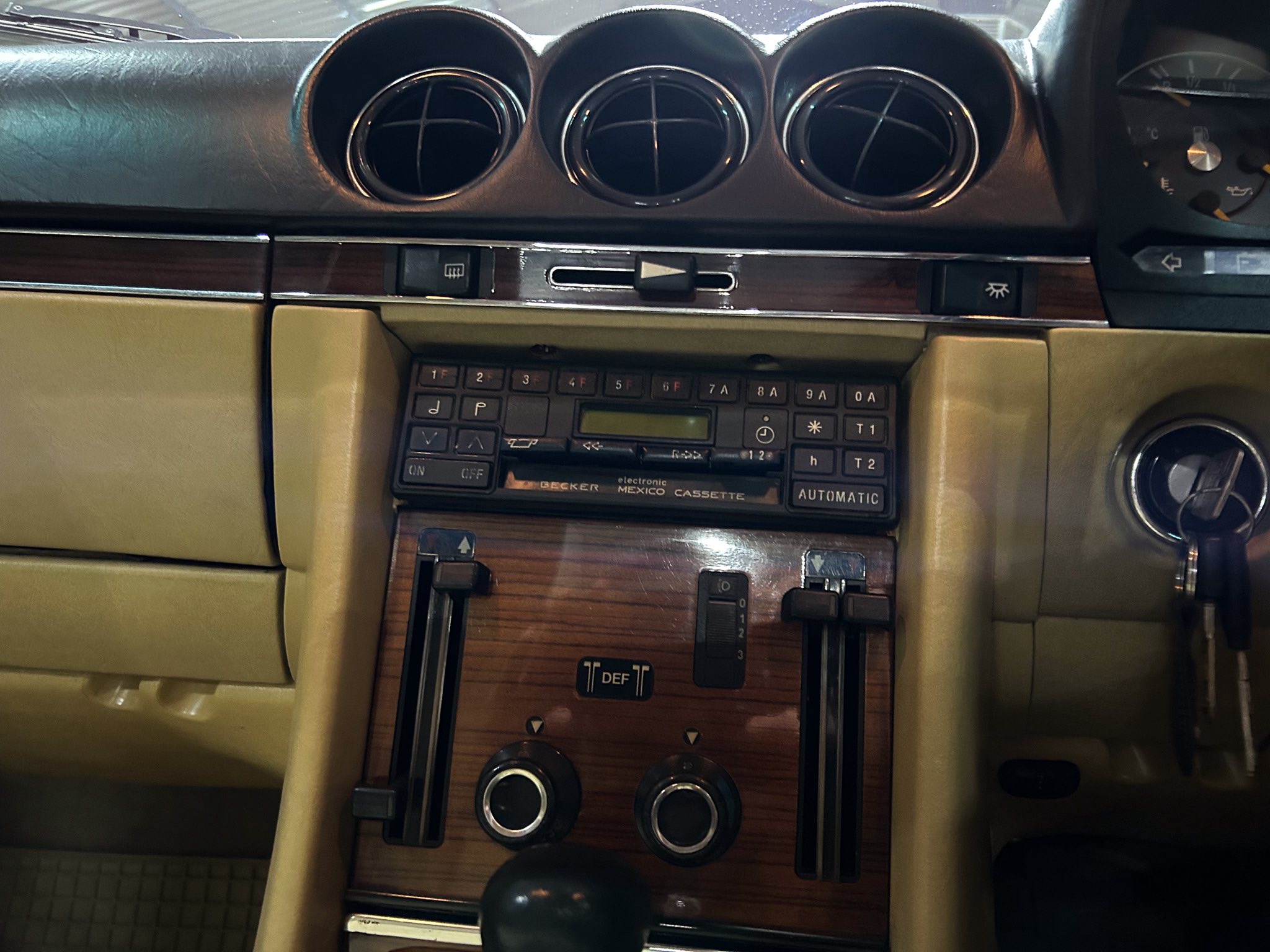 Car interior center dashboard with three circular air vents above a wood-grain panel and cassette deck.