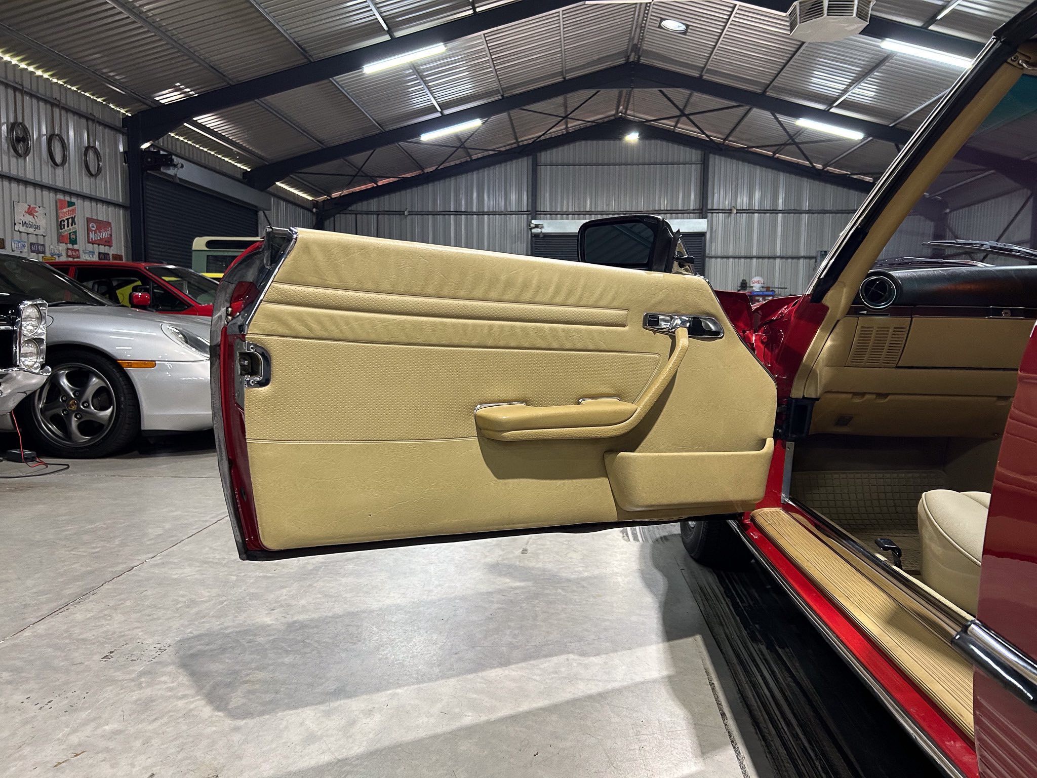 Beige interior door panel of a vintage convertible with red exterior in a metal-walled garage.