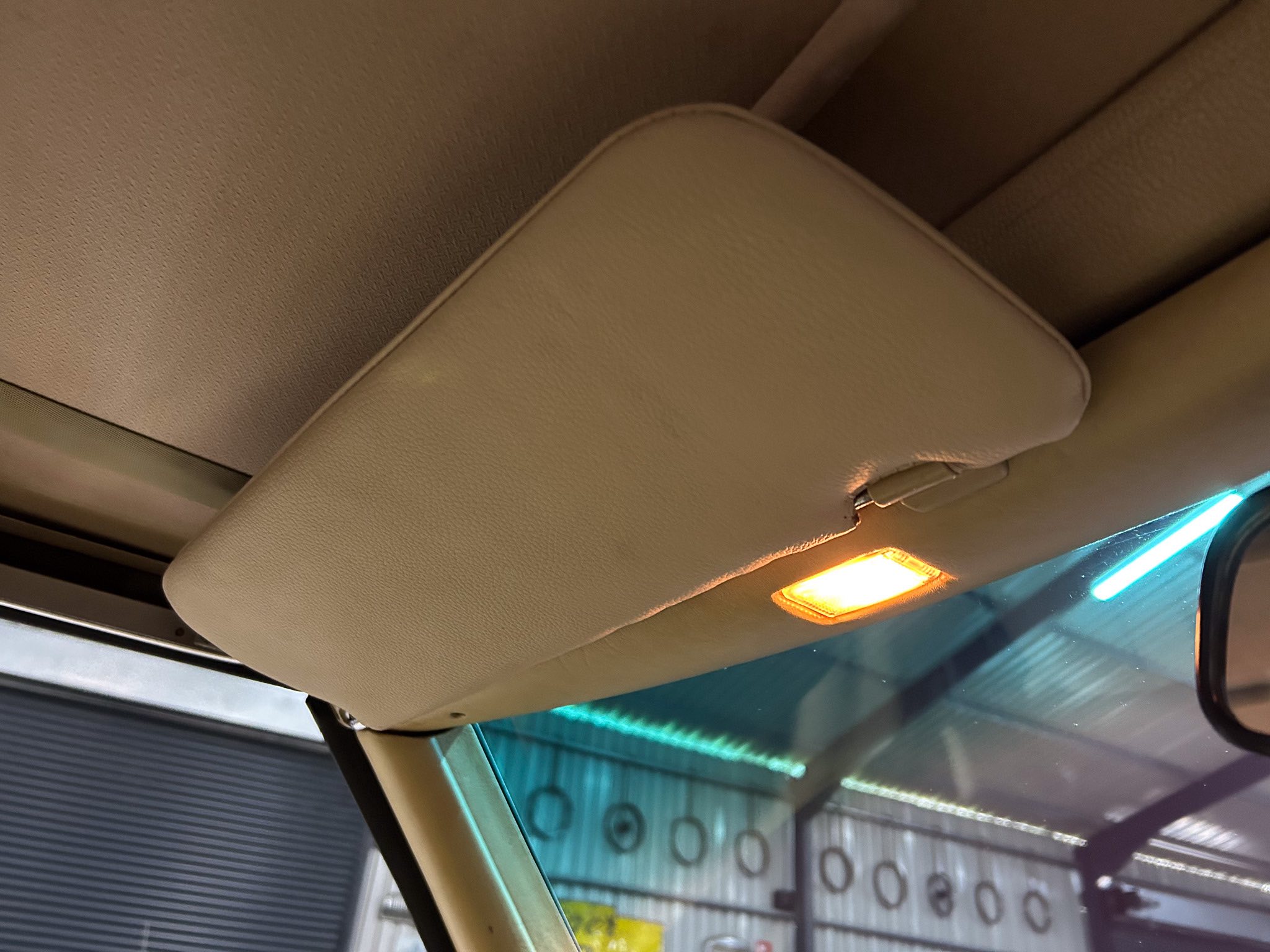 Beige car headliner with a small overhead light, sun visor edge visible, through a side window.