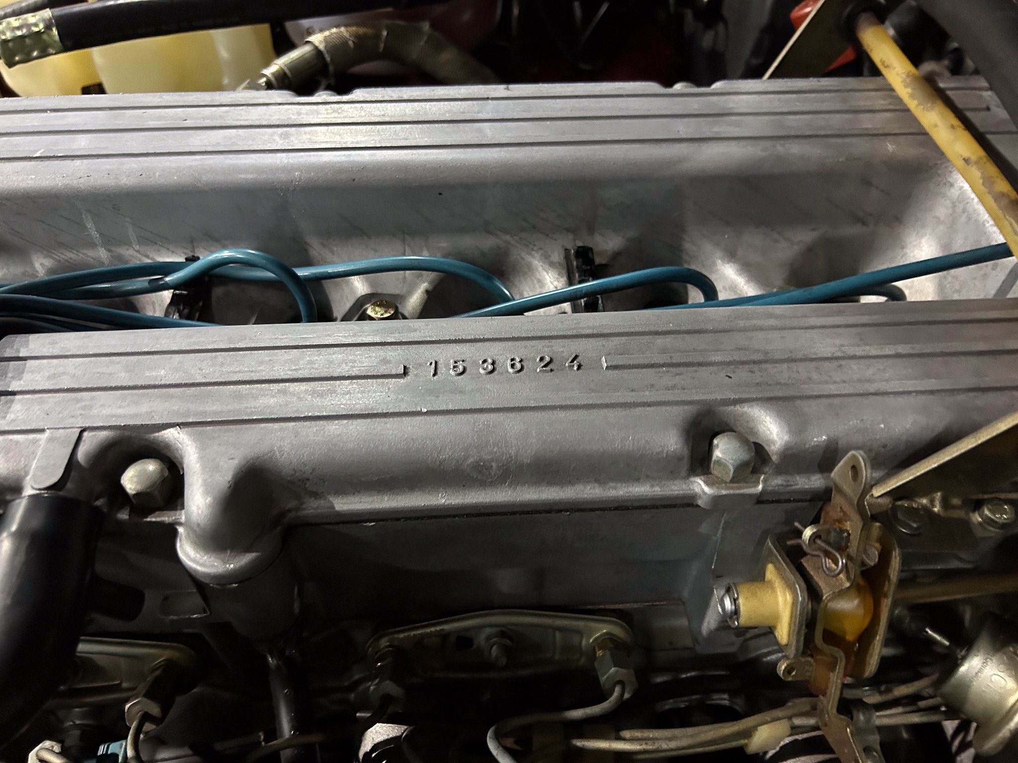 Close-up of a car engine bay showing blue wiring harnesses and a stamped number 153624 on a metal housing.