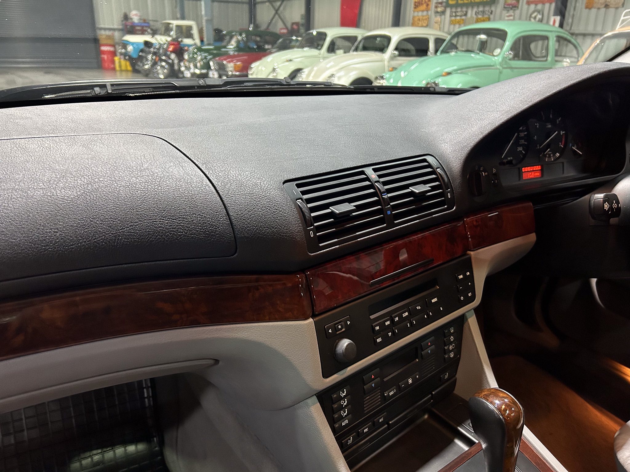 Interior of a car dashboard with vents and wood trim, view of classic cars outside a showroom through the windshield