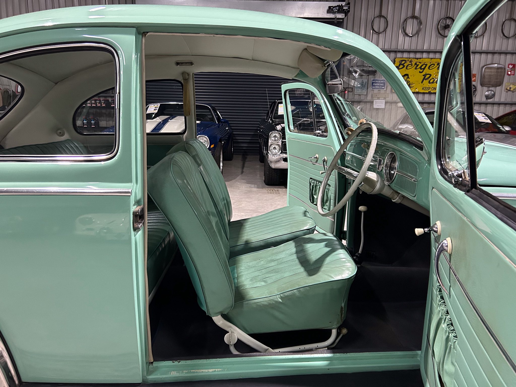 Open mint-green vintage car with its door ajar, showing green upholstery and chrome trim inside a showroom. Recessed seats and steering wheel visible in a classic car interior.