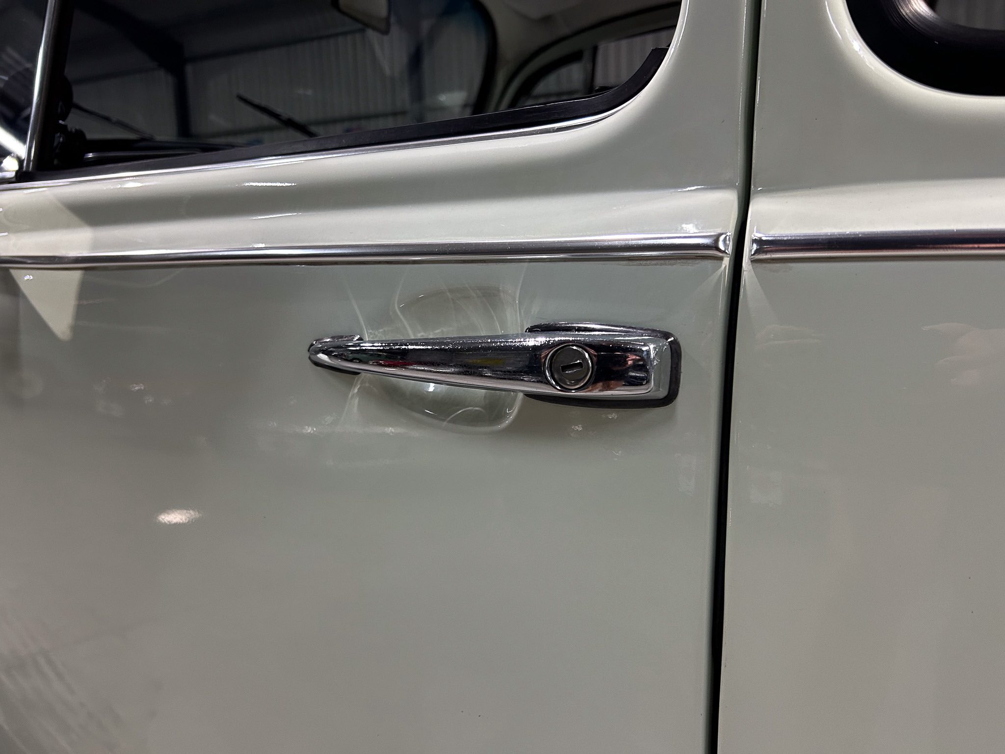 Close-up of a vintage car door with a chrome handle and trim along the panel edge.