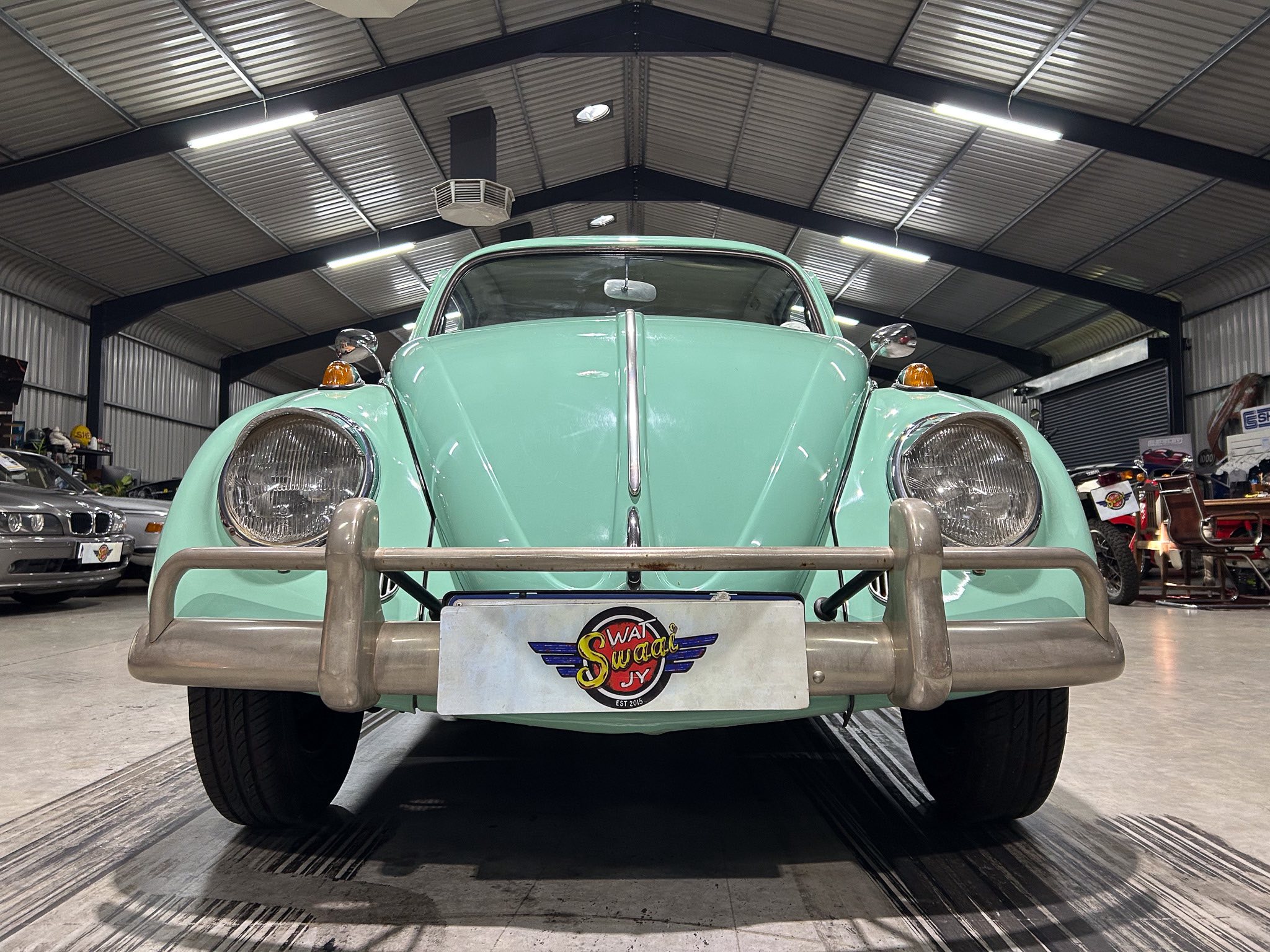 Front view of a mint green vintage car in a showroom, featuring a chrome bumper, round headlights, and a 'Swag' license plate logo.