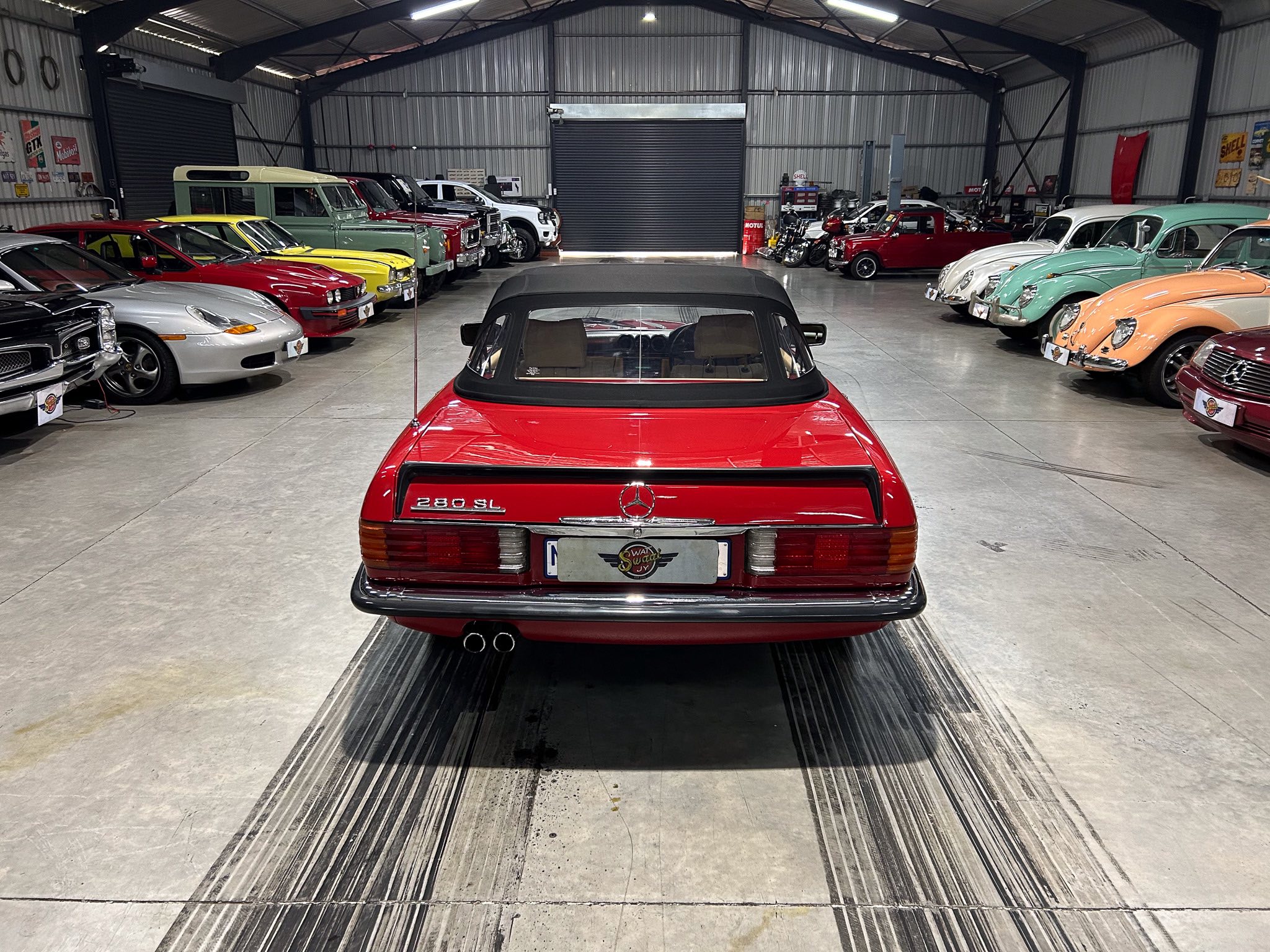 Rear view of a red Mercedes 280SL with a black convertible top in a vintage car showroom.