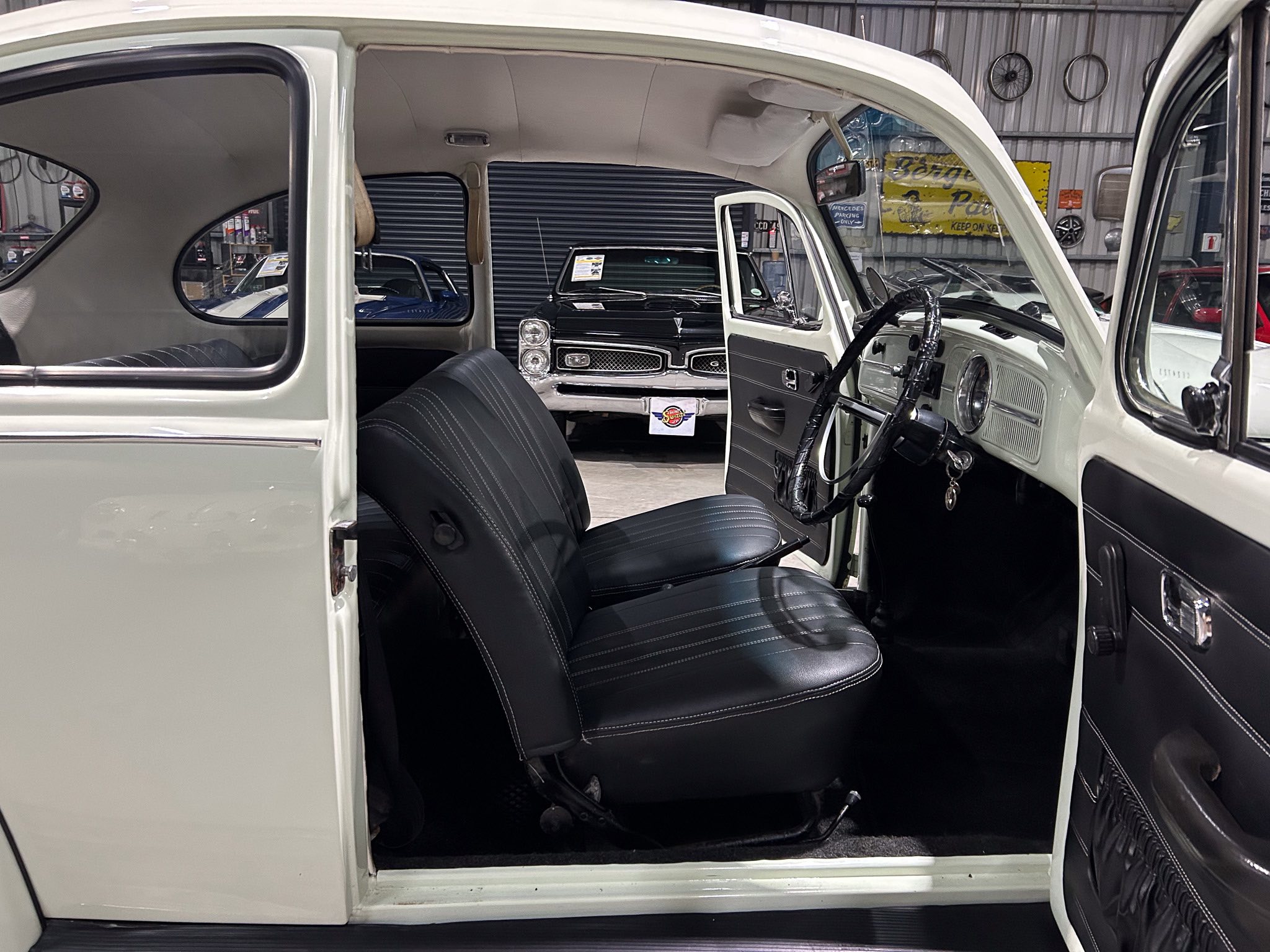 Open-door view of a vintage car interior with black seats and chrome accents in a showroom.