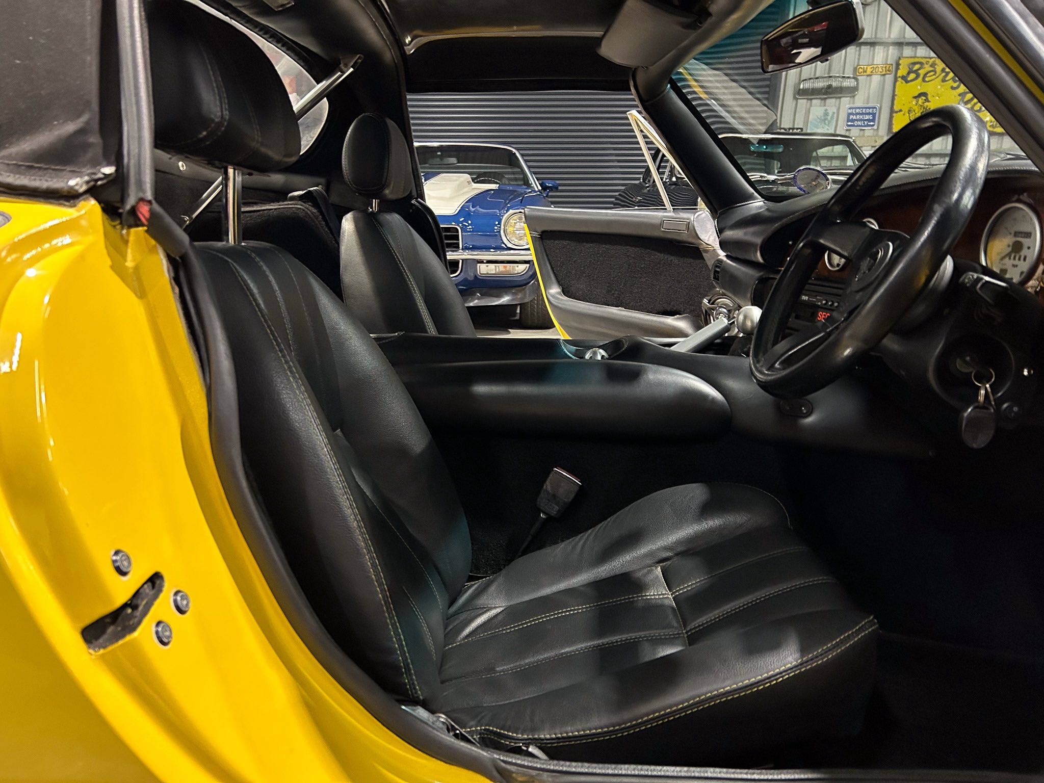 Interior of a yellow sports car with black leather seats and a right-hand drive steering wheel, viewed from the passenger side edge of the door open long shot.